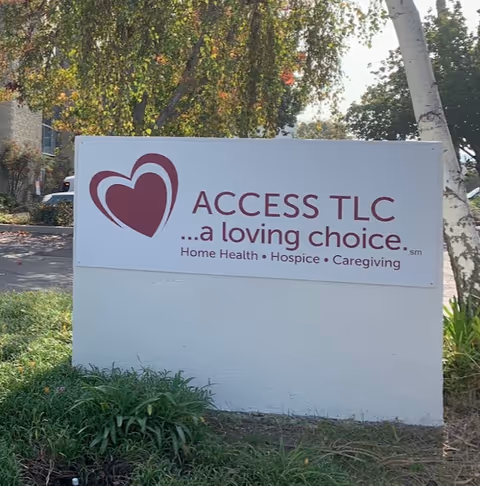 A large white Access TLC sign with a heart logo sits in front of greenery.