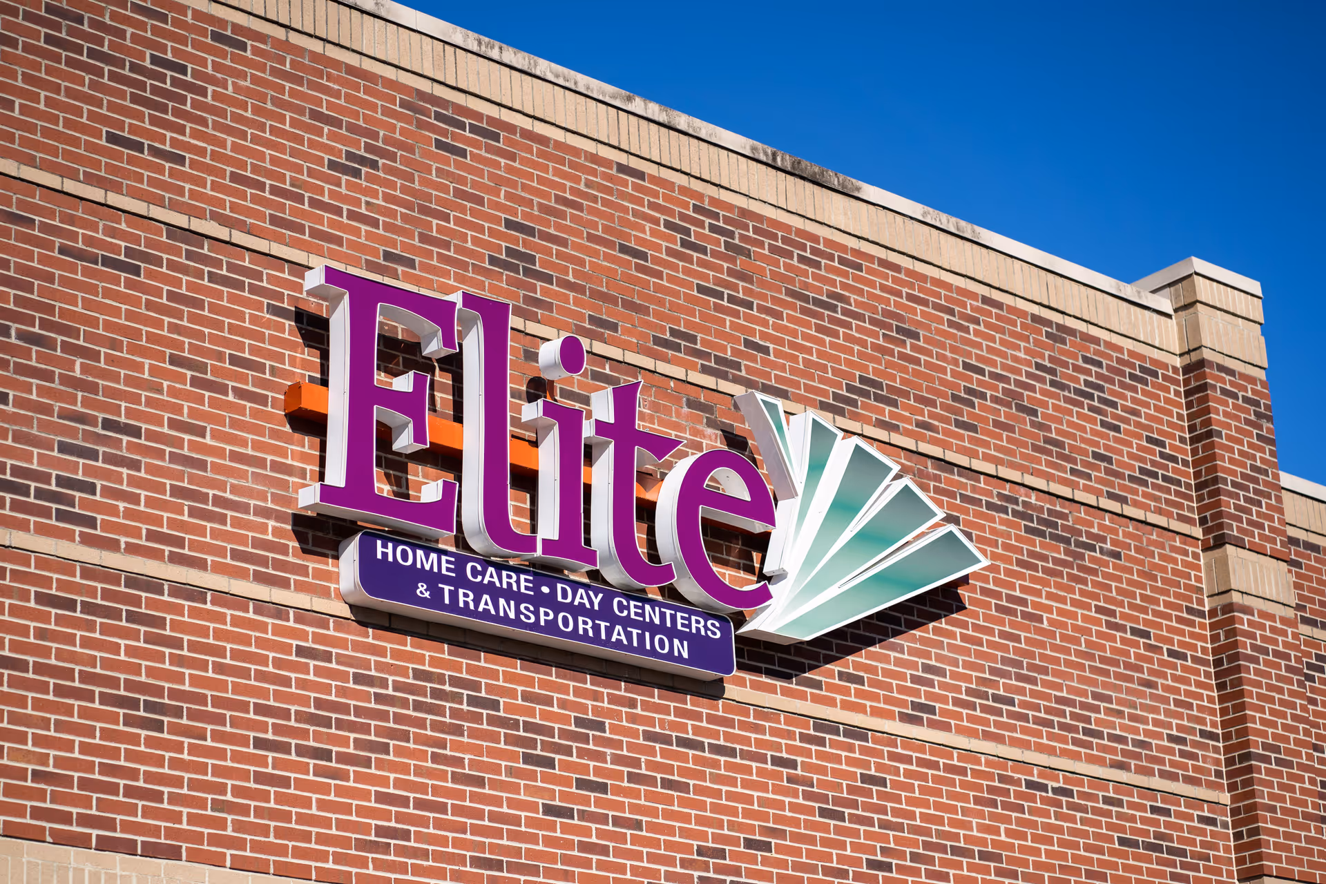 Brick building exterior with a large Elite sign advertising home care and transportation.