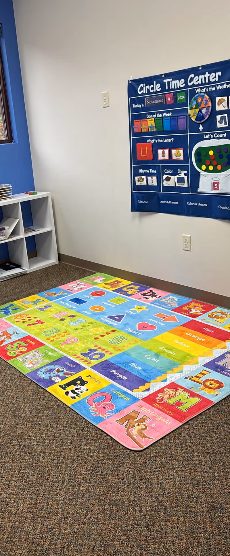 Colorful Alphabet rug on carpeted floor beside Circle Time Center poster.