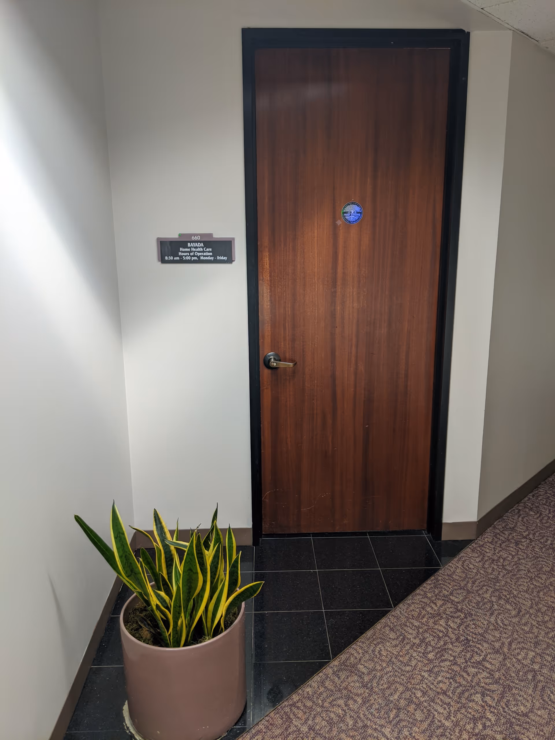 Hallway interior with a wooden door, wall plaque, and potted plant.