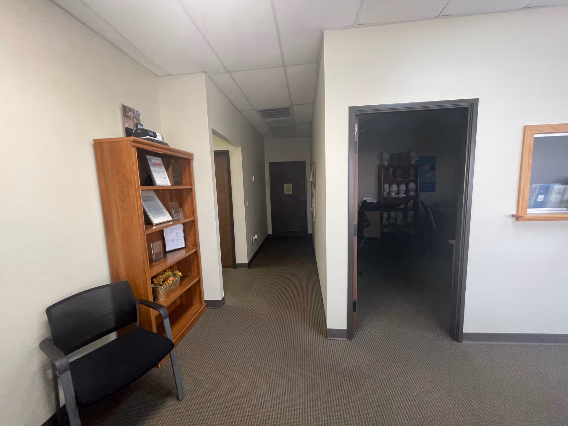 Empty hallway inside a senior facility with a chair and wooden bookshelf.