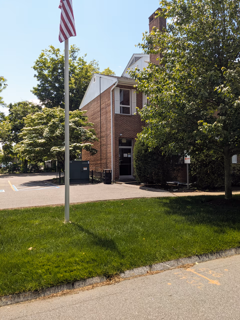 Brick senior living facility entrance with flagpole, trees, and a sidewalk