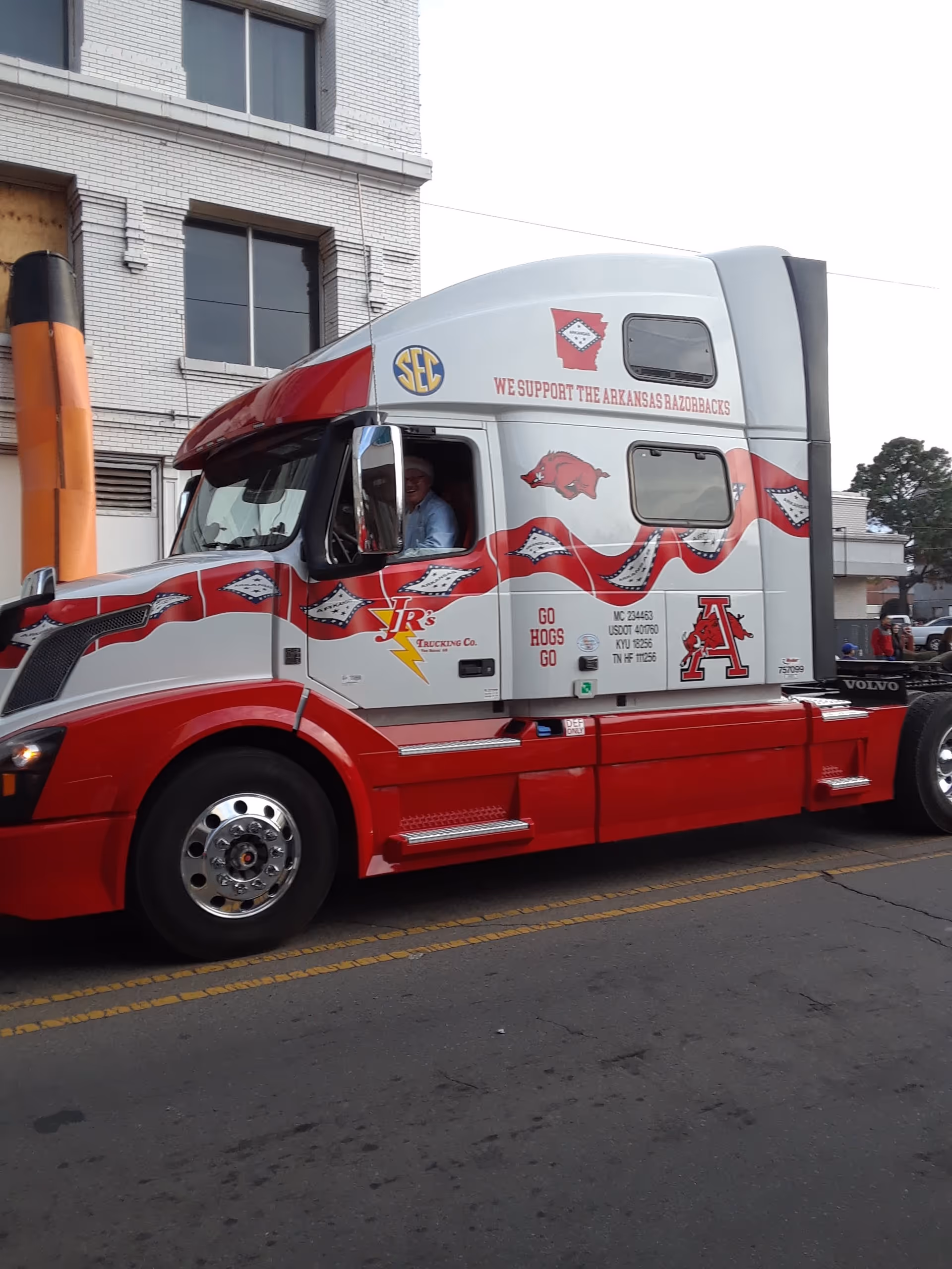Red and white Arkansas Razorbacks semi truck driving on a city street beside a brick building
