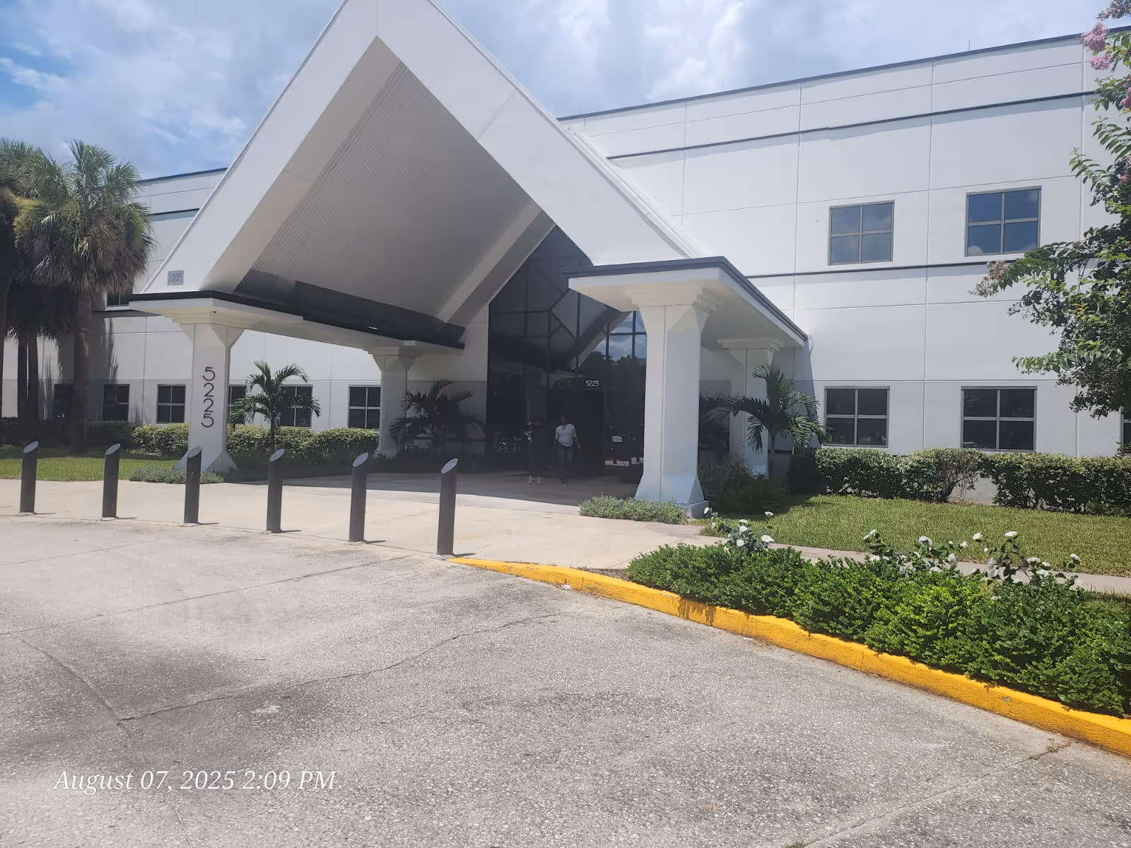 Exterior view of a white senior living facility with a tall angled entrance canopy.