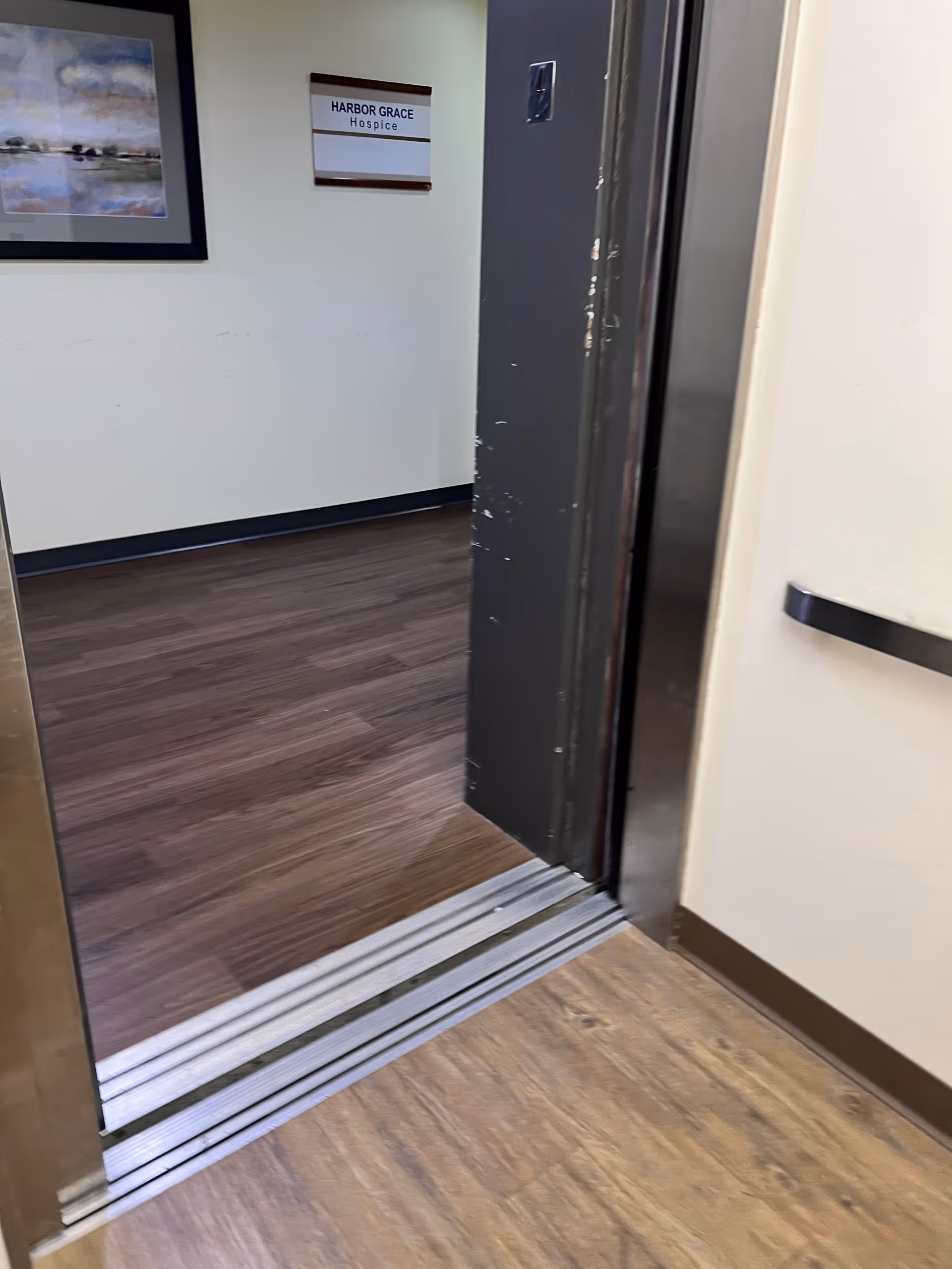 Open elevator doors in a hallway with Harbor Grace Hospice sign on the wall.