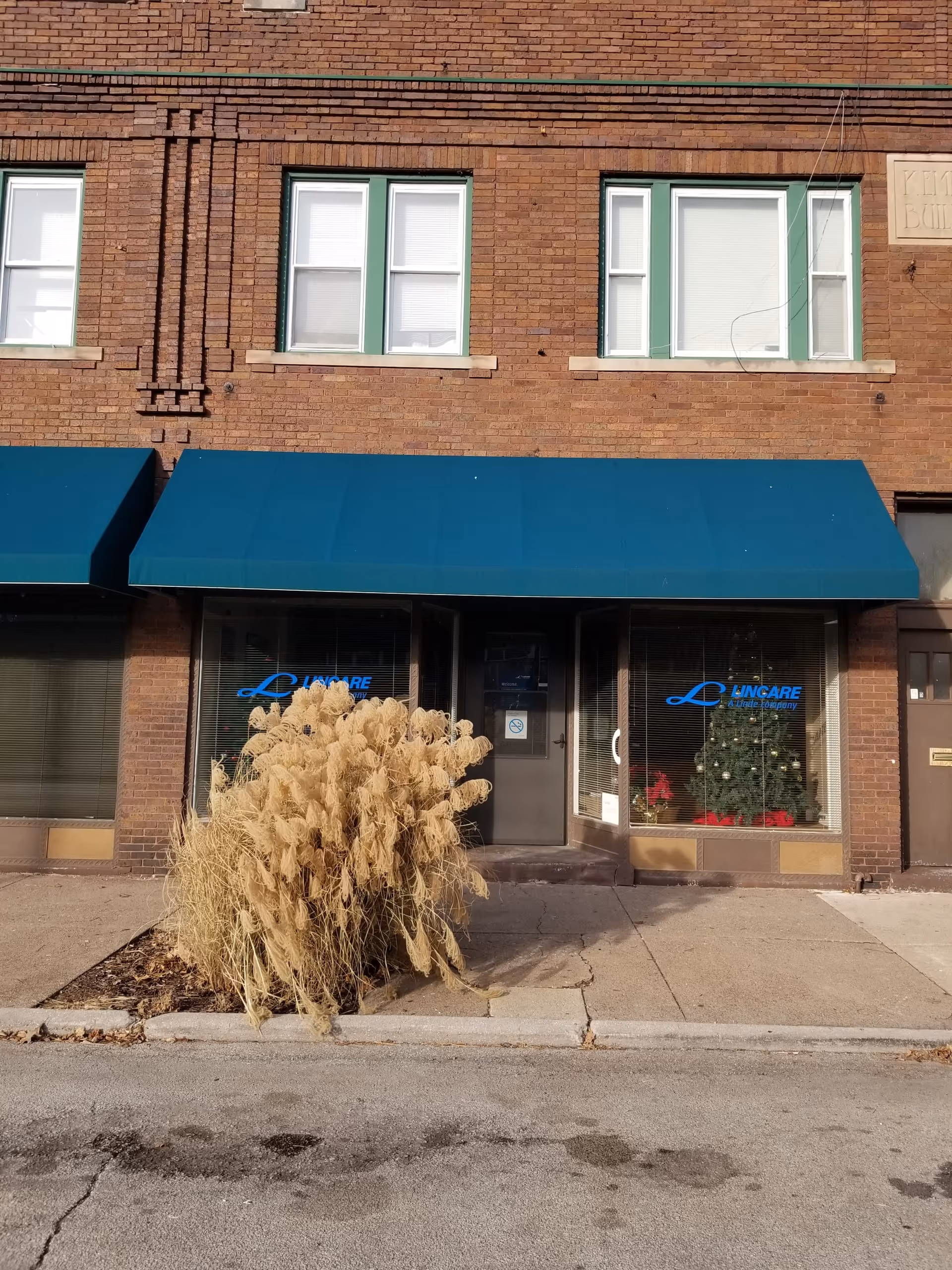 Brick building with blue awnings and Lincare storefront windows along the sidewalk.