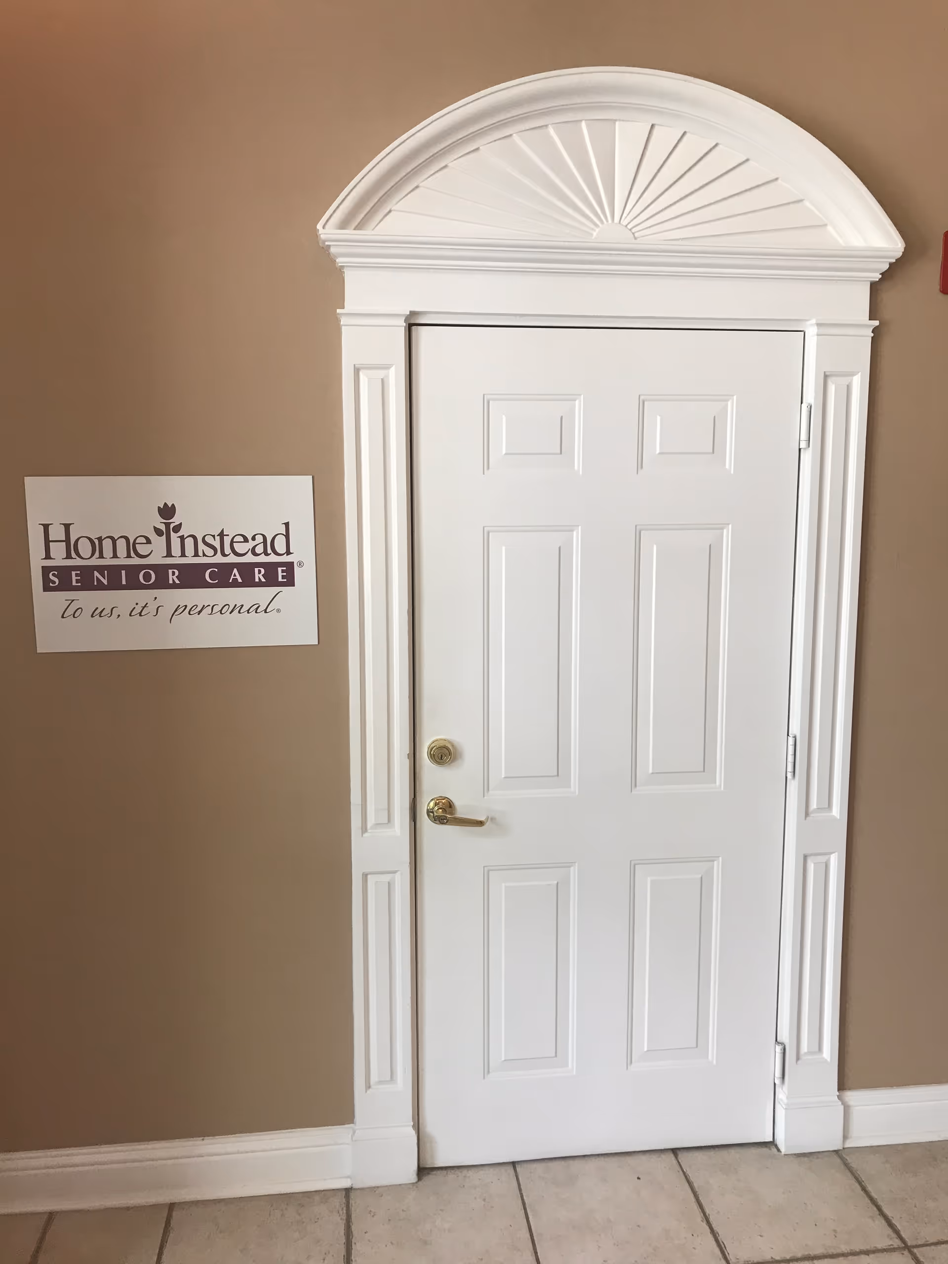 White decorative door with arch-top molding in beige hallway, Home Instead sign beside it.