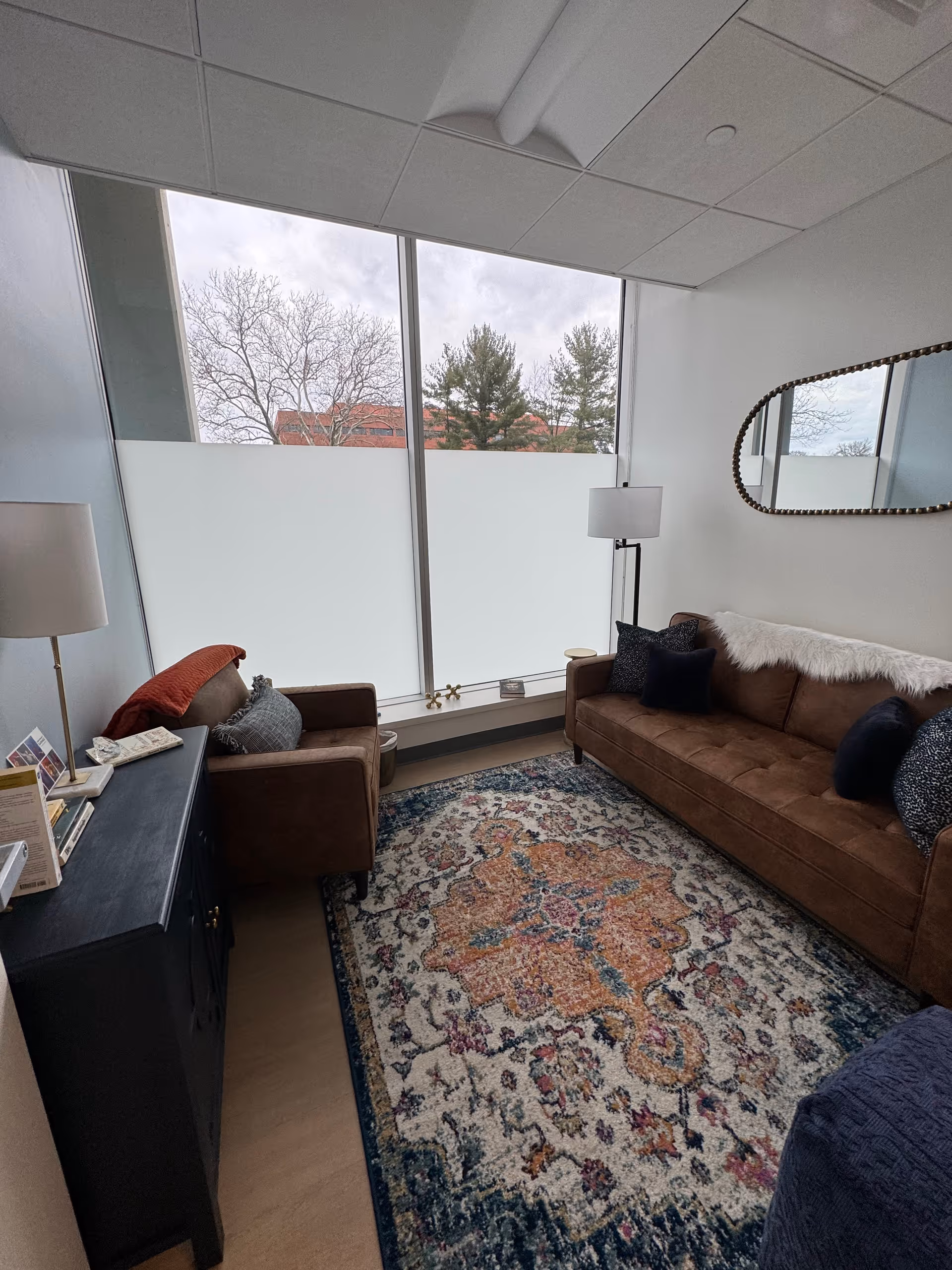 Cozy living room with brown sofa, armchair, rug, and large frosted windows.