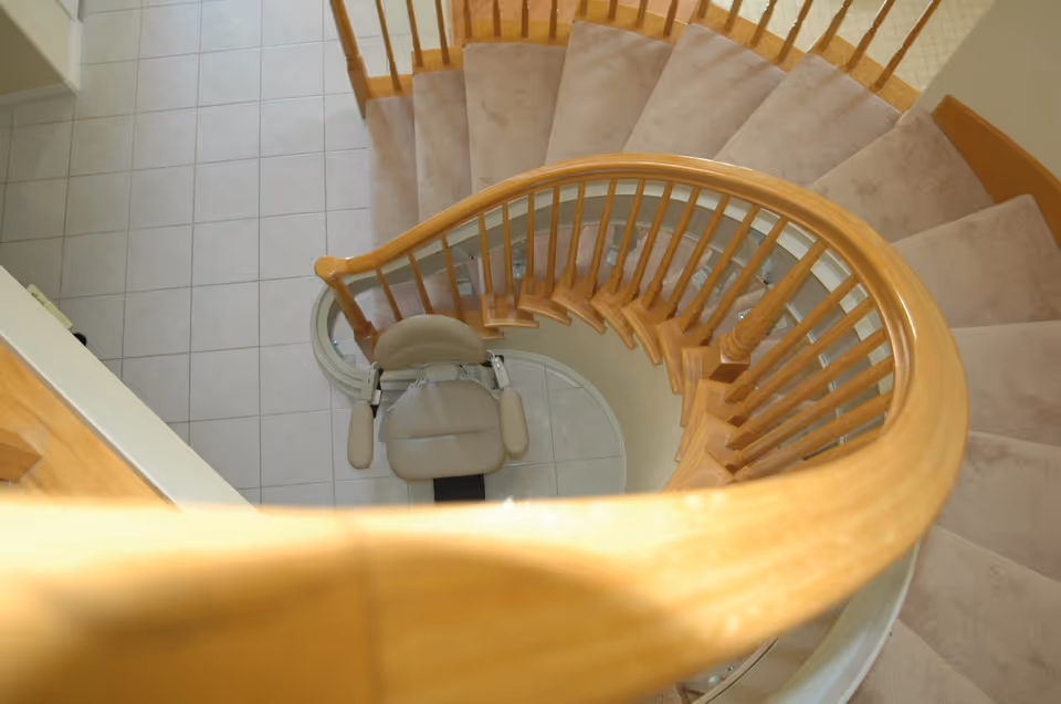 Overhead view of a curved wooden staircase with a beige stairlift chair at the center.