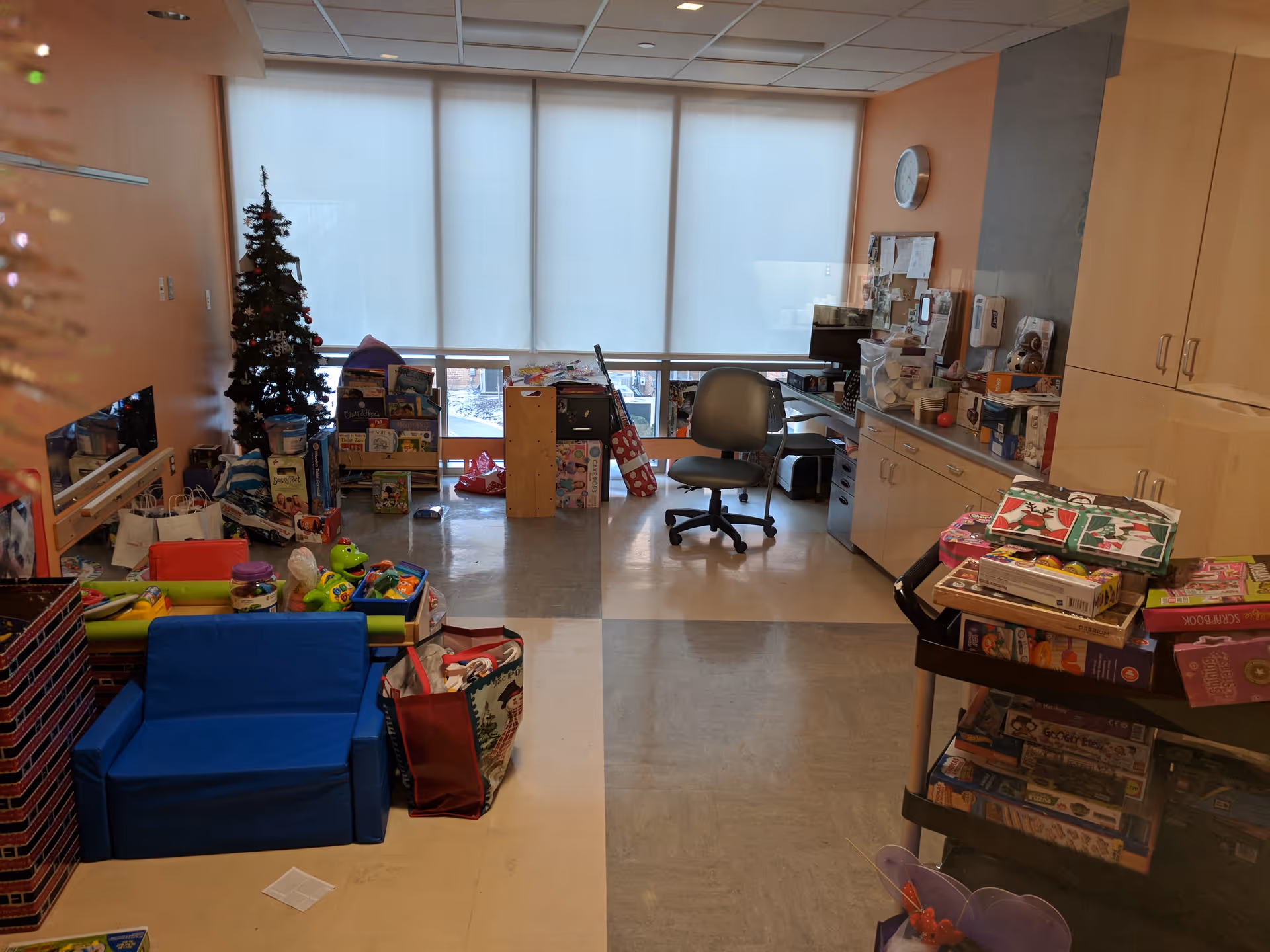 Indoor play area with toys, a Christmas tree, desk, and large windows.