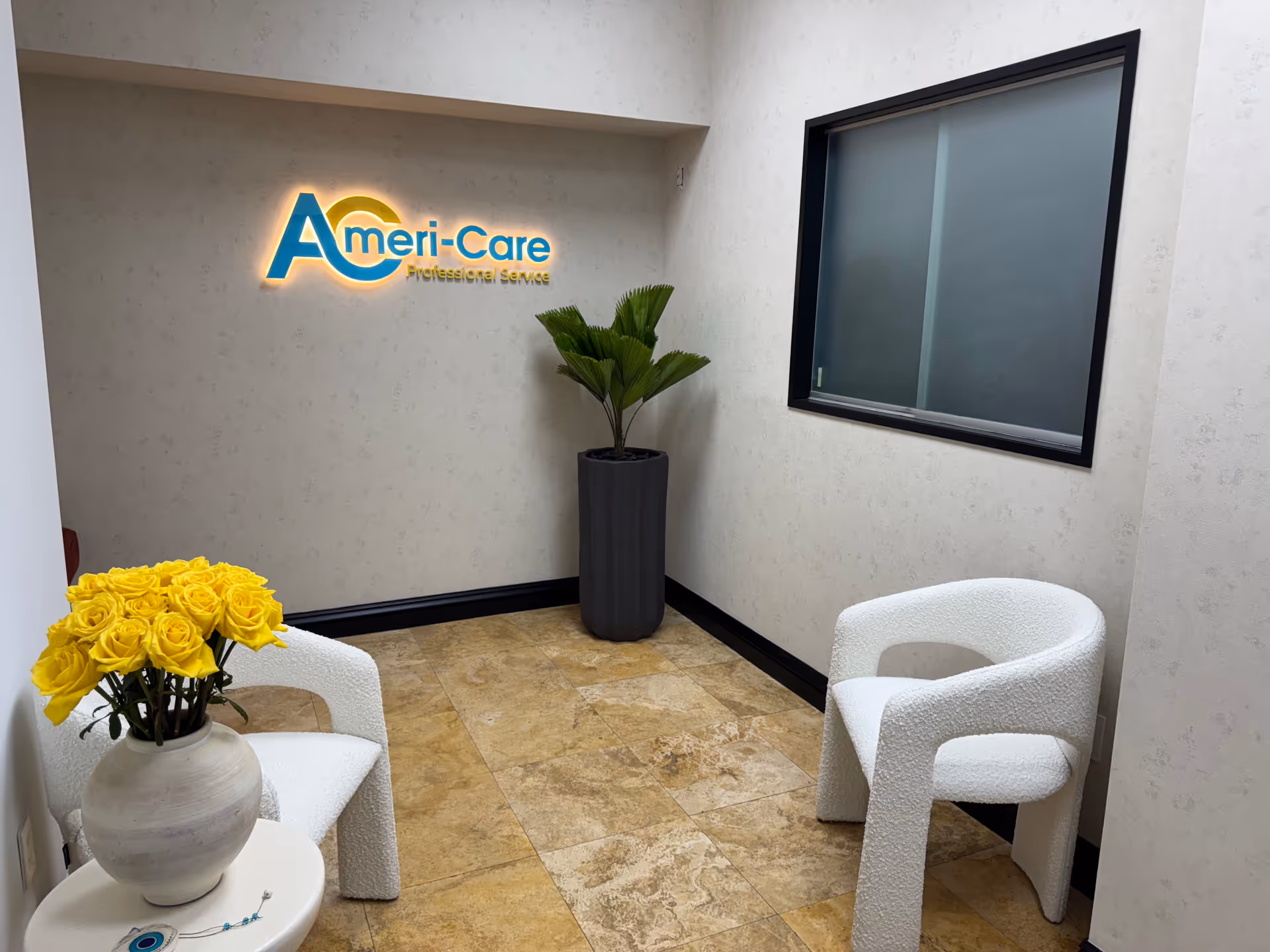 Interior waiting area with cream walls, yellow roses, white chairs, and Ameri-Care sign.