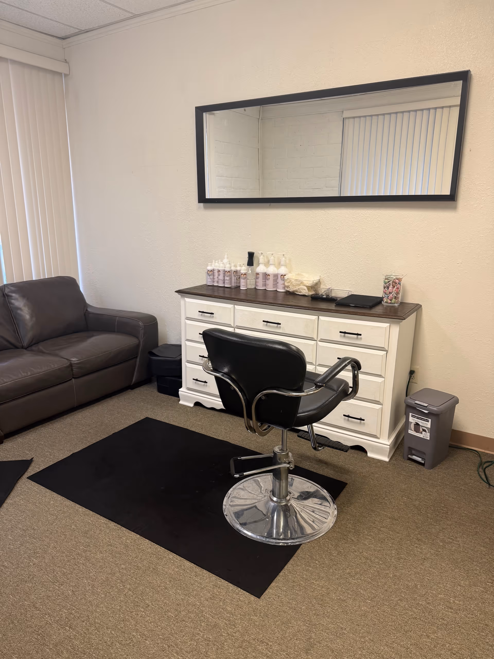 A compact salon area with a styling chair, dresser, mirror, and couch.