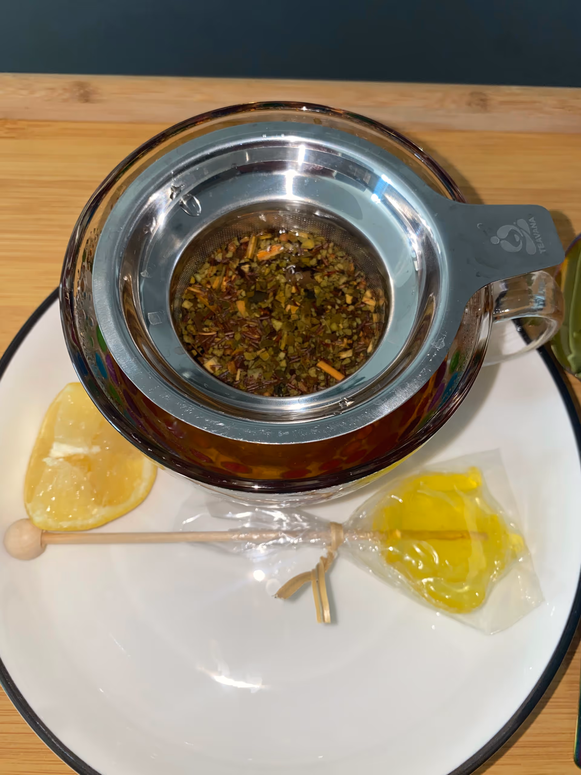 Close-up of a metal tea infuser in a teapot with lemon wedge on a plate.