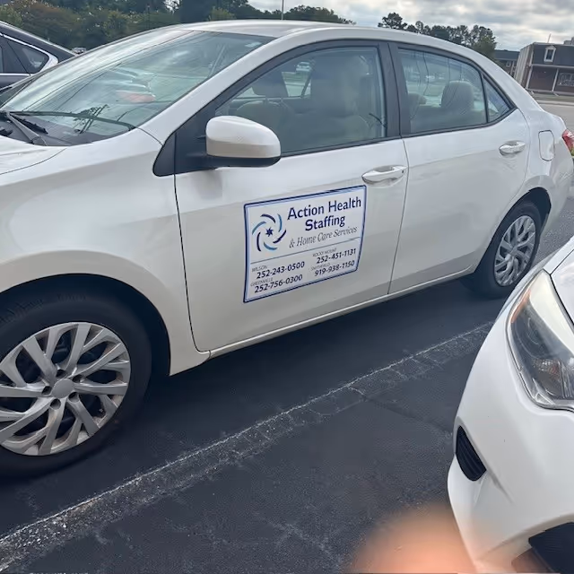 White sedan in a parking lot with Action Health Staffing logo on the door.