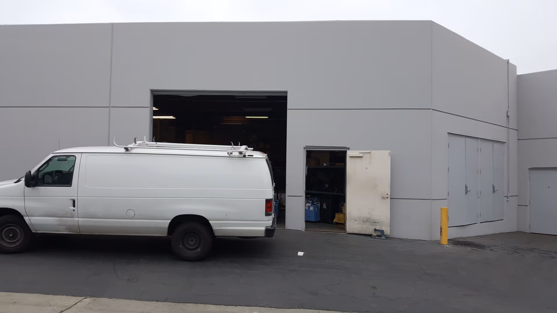 Exterior view of a gray industrial building with a white van parked near a loading bay.