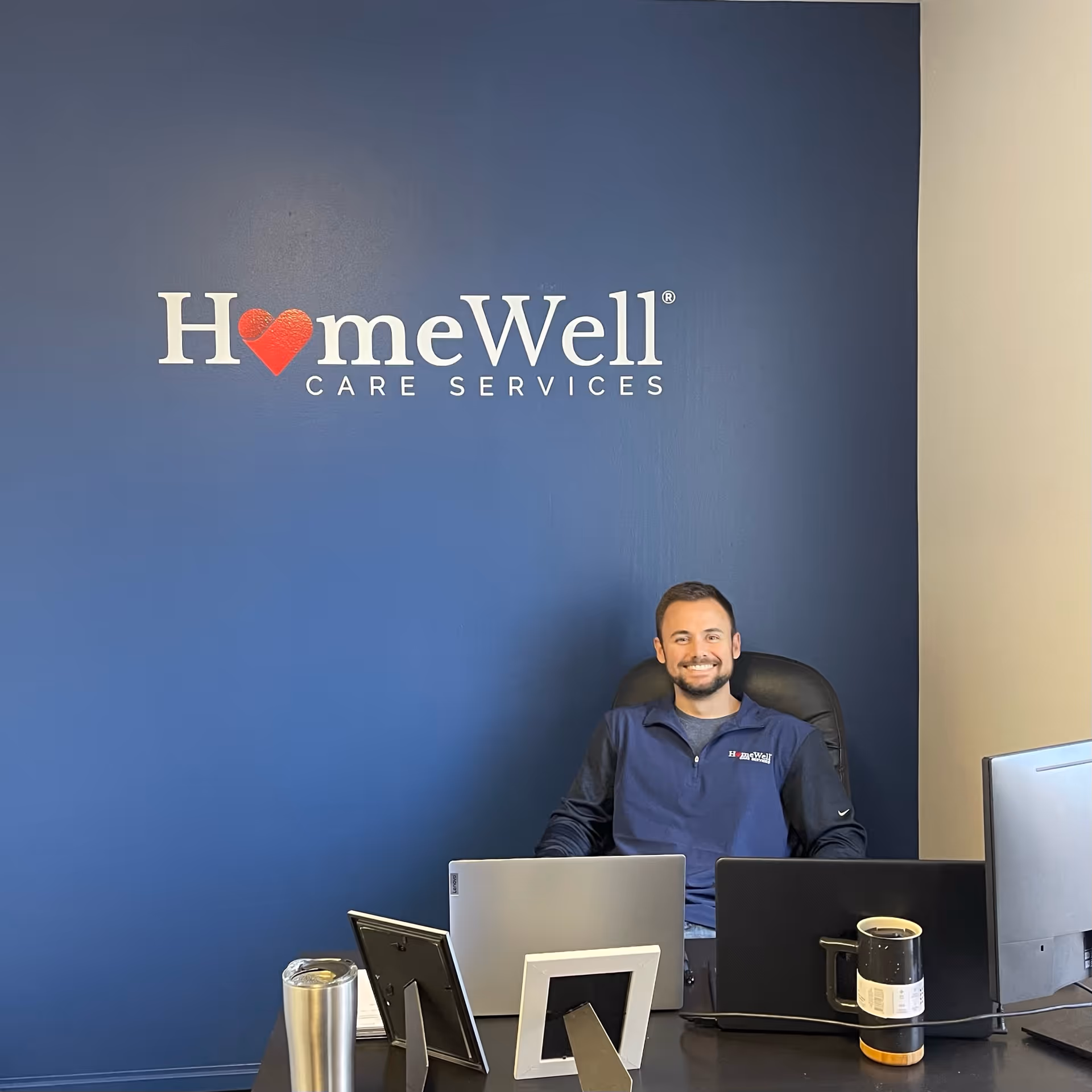 Smiling man sits at a desk in a HomeWell Care Services office.