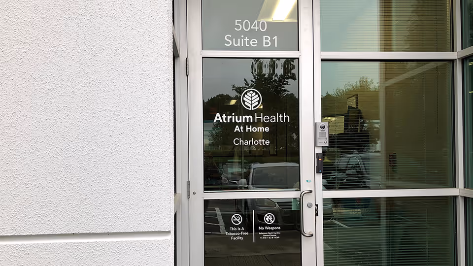 Glass entrance with Atrium Health At Home Charlotte branding and Suite B1 label.