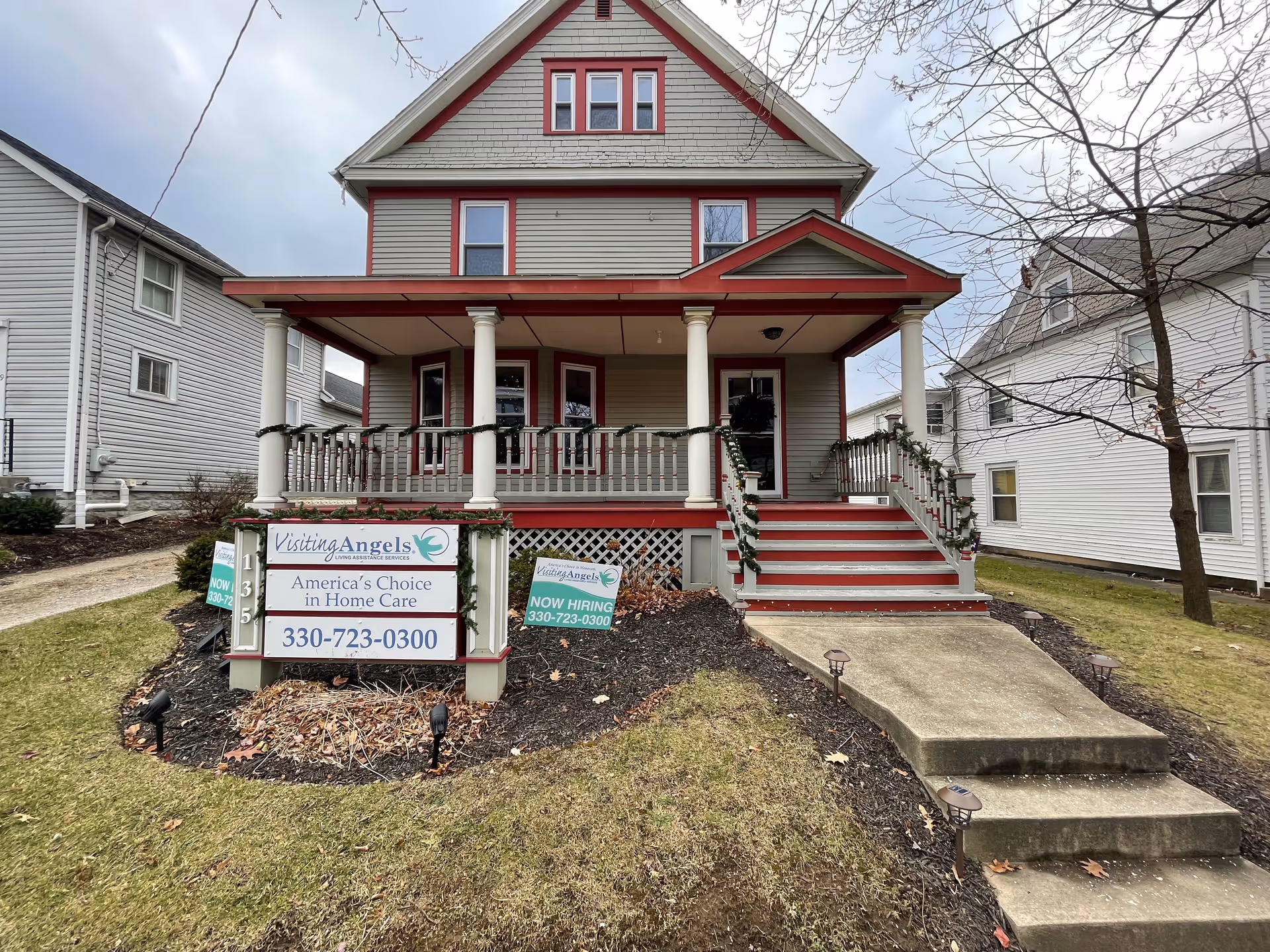 Two-story home with a red-trimmed porch and Visiting Angels signs.