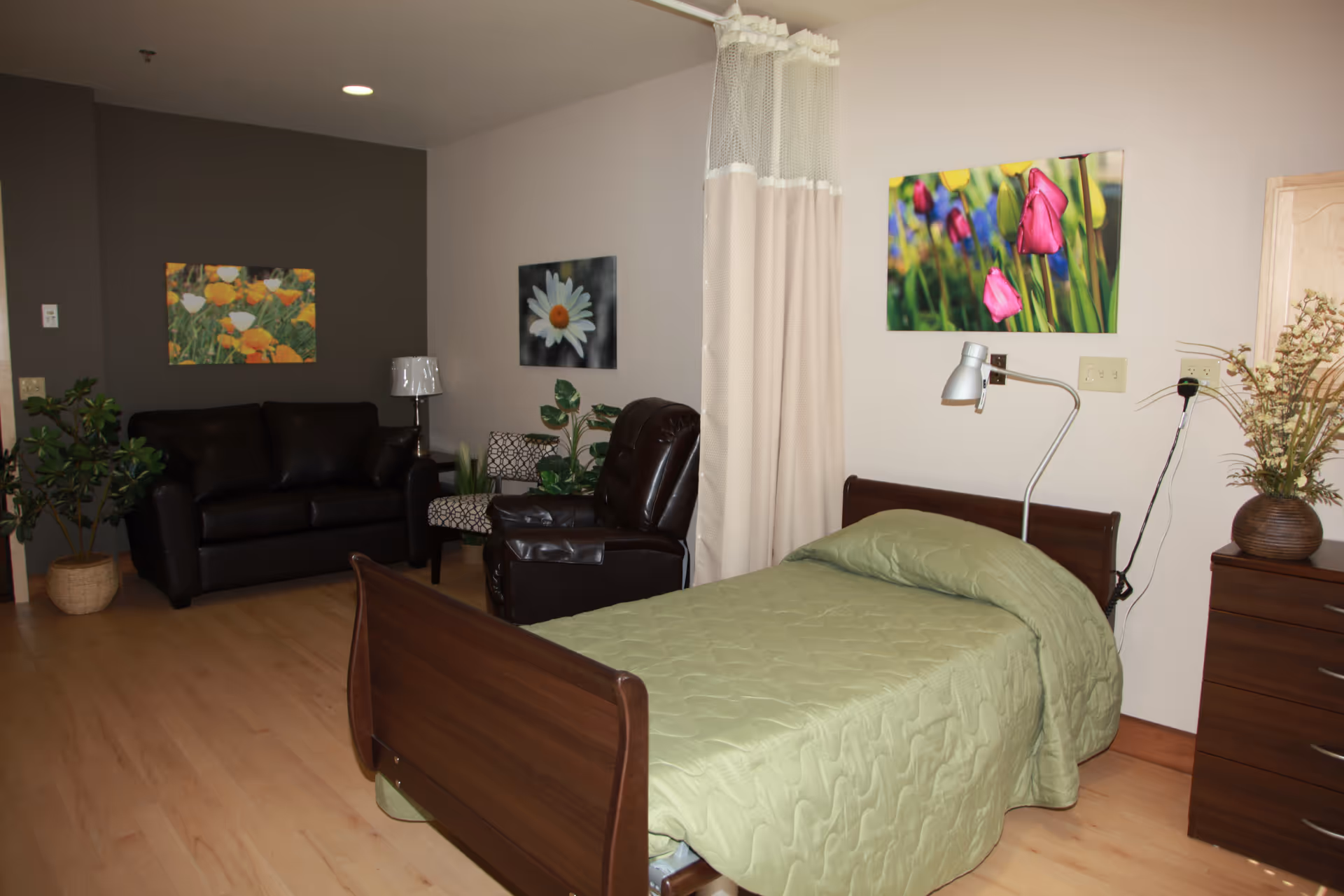 Senior living facility bedroom with a green quilted bed and lounge seating area.