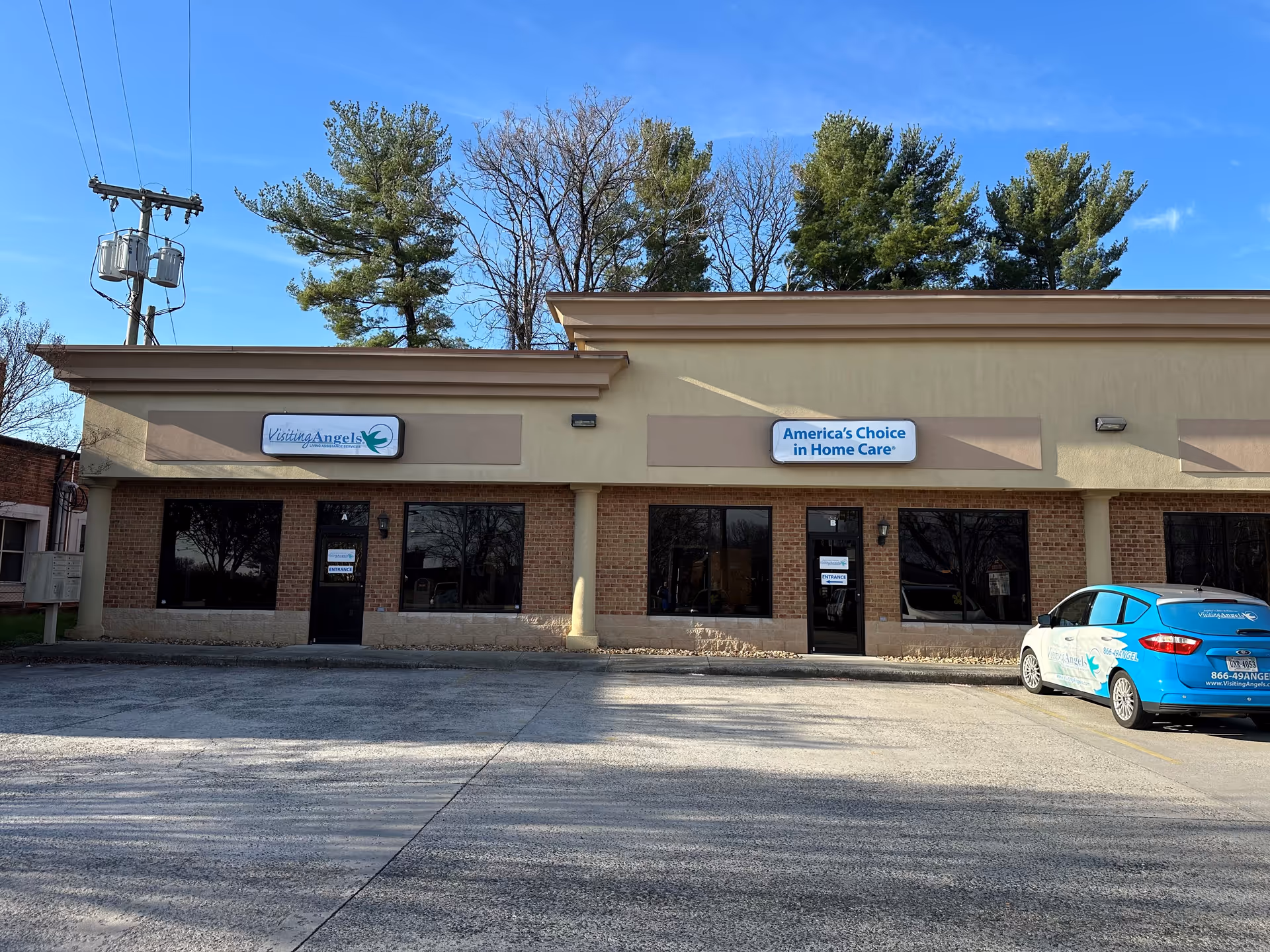 Exterior view of a beige building with Visiting Angels signage and a blue car in lot.