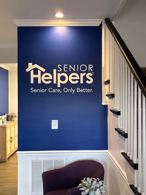 Blue wall displays Senior Helpers logo beside a staircase in an indoor hallway.