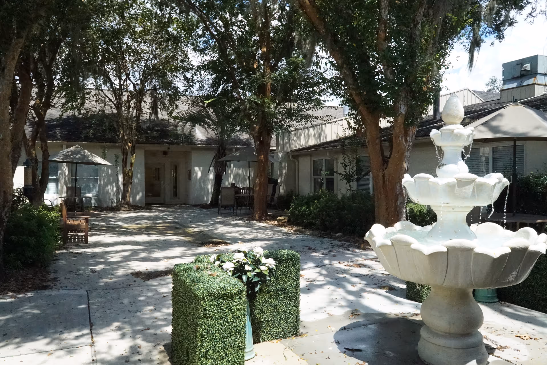 Sunlit outdoor courtyard with a large tiered fountain, trees, and seating.