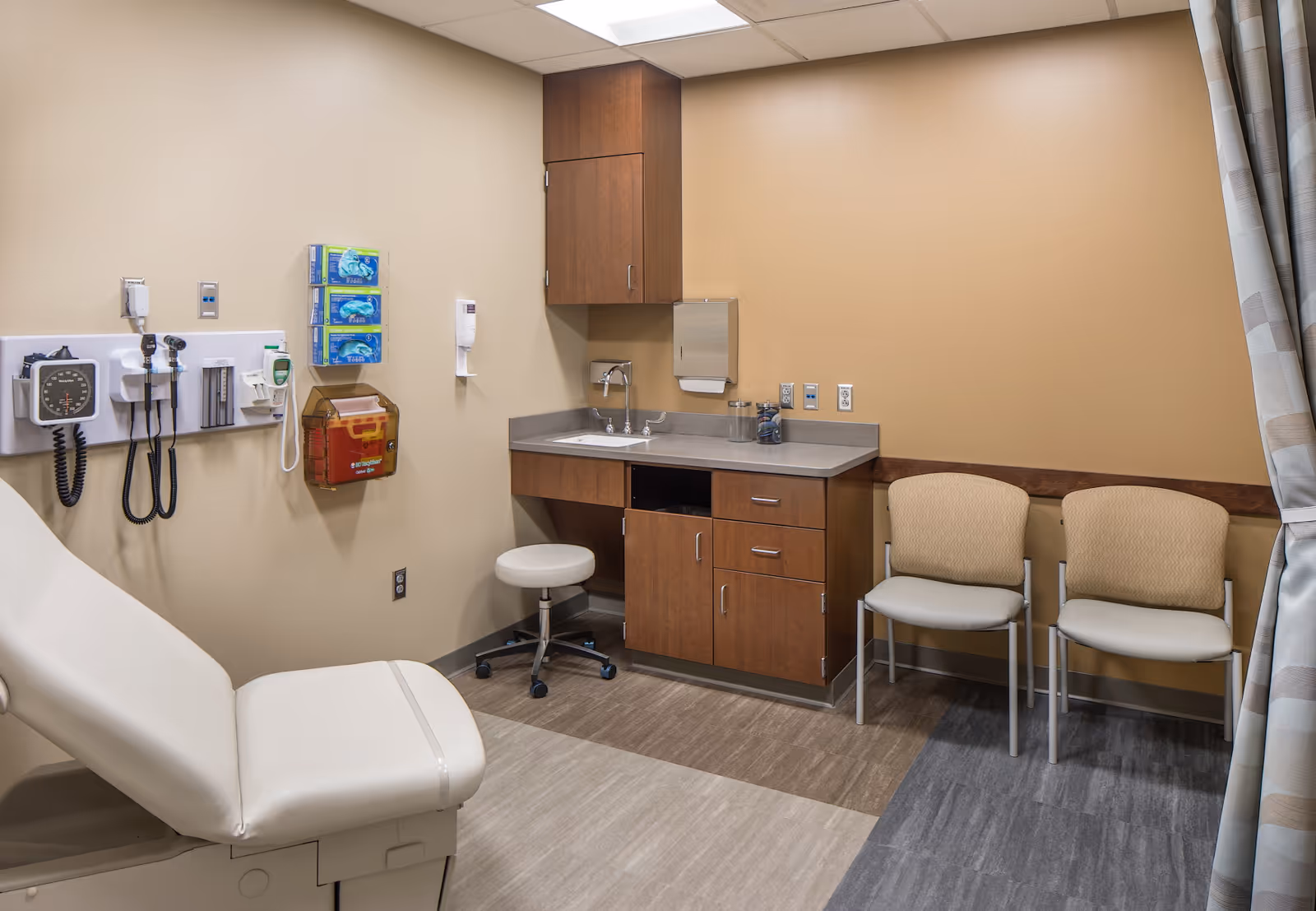 A medical examination room with exam chair, sink, and storage cabinets.
