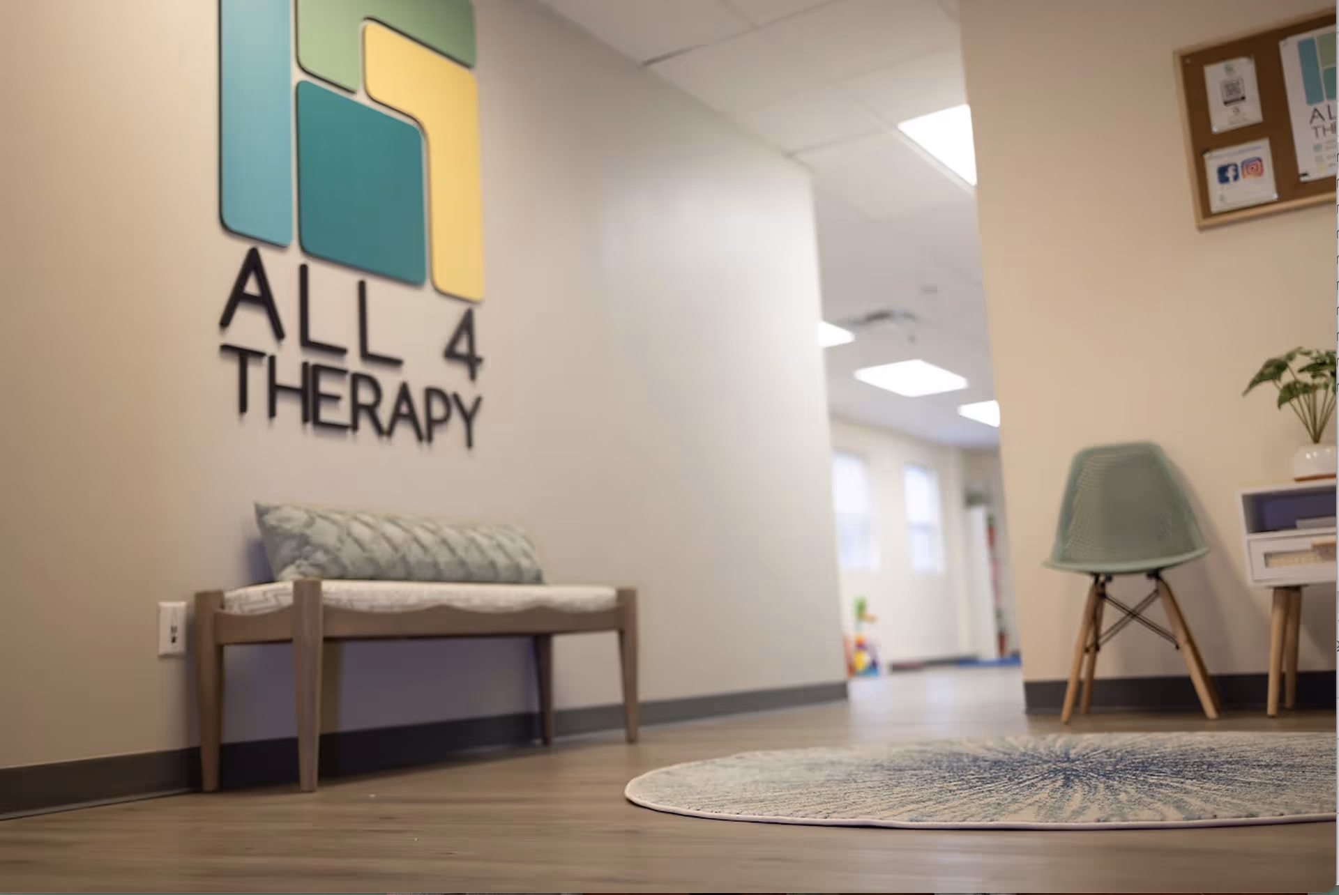Interior hallway featuring All 4 Therapy logo, a bench, and a teal chair.