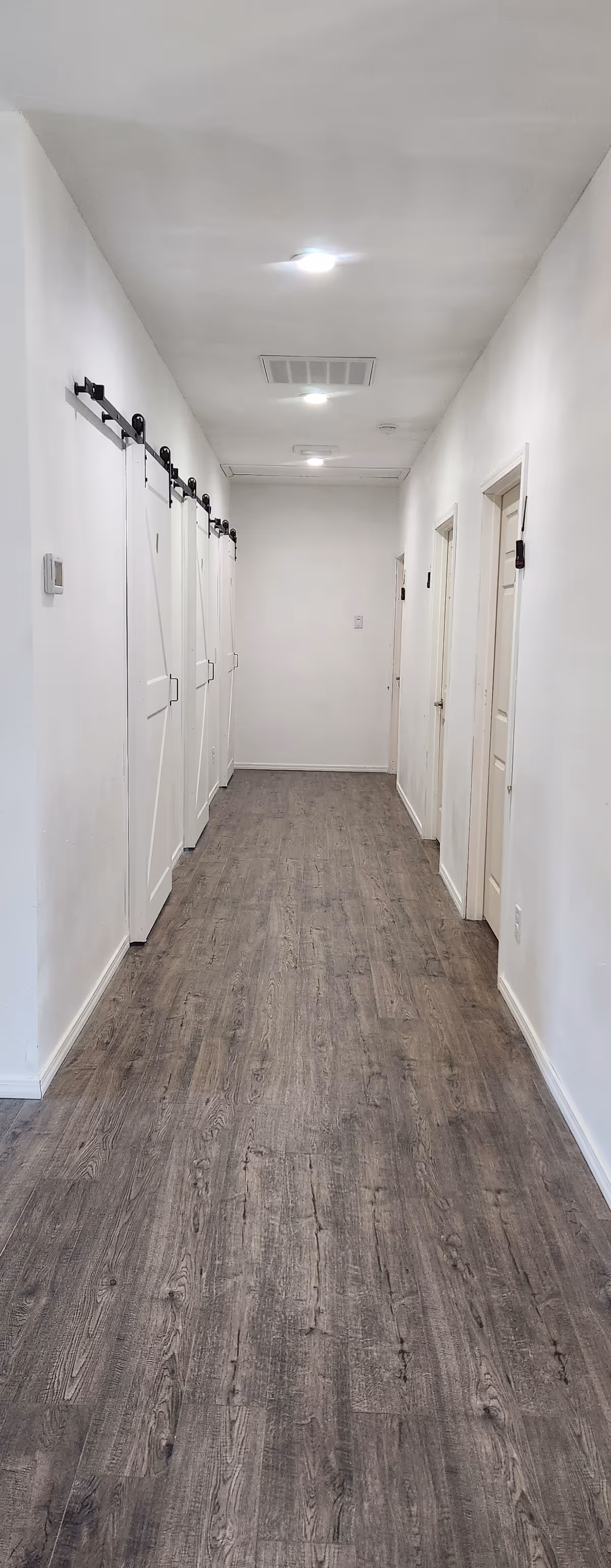 Long white hallway in a senior living facility with closed doors along both sides.