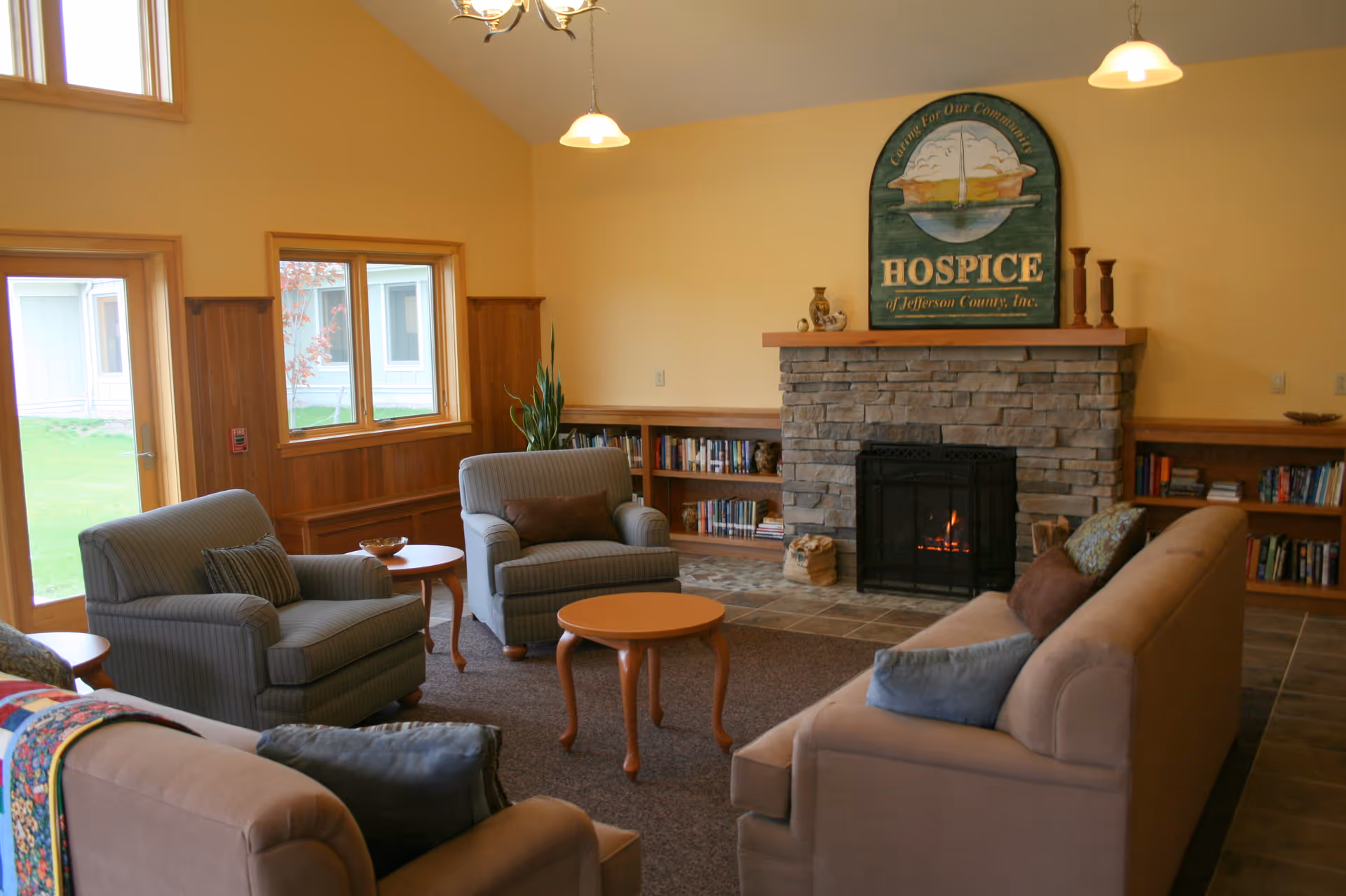 Cozy lounge with a stone fireplace, comfortable seating, and a Hospice sign.
