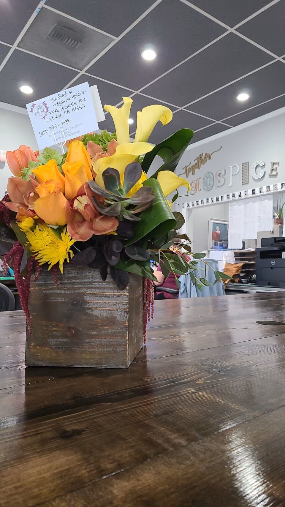 Floral centerpiece on a wooden table in hospice reception.