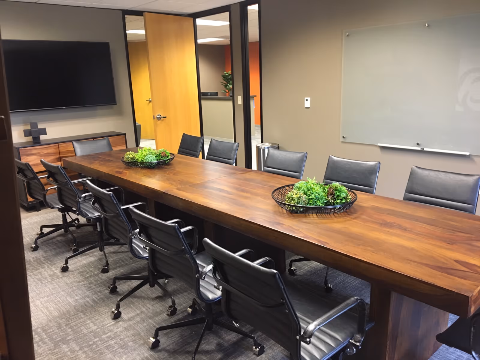 A long wooden conference table with black chairs in a modern meeting room.