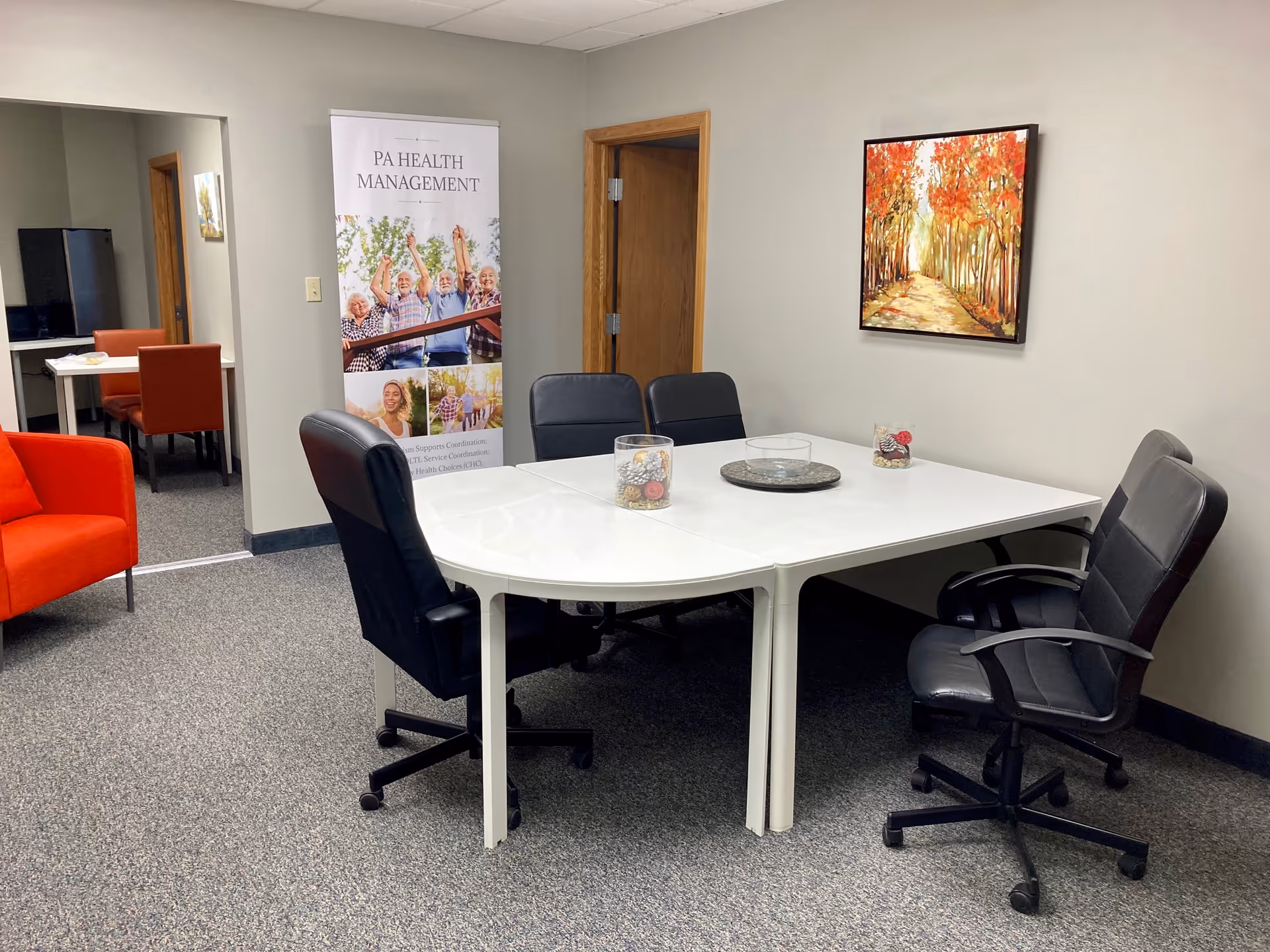 A white conference table with black chairs sits in a beige-walled interior meeting room.