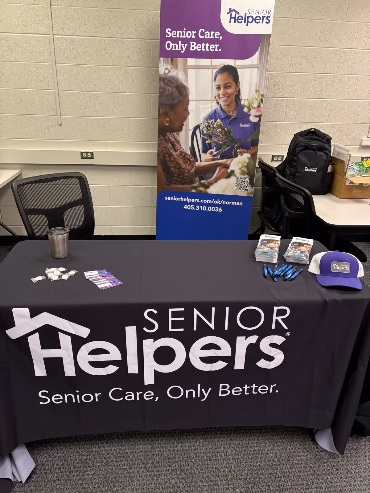 Indoor promotional table for Senior Helpers with banner, brochures, pens, and a cap.
