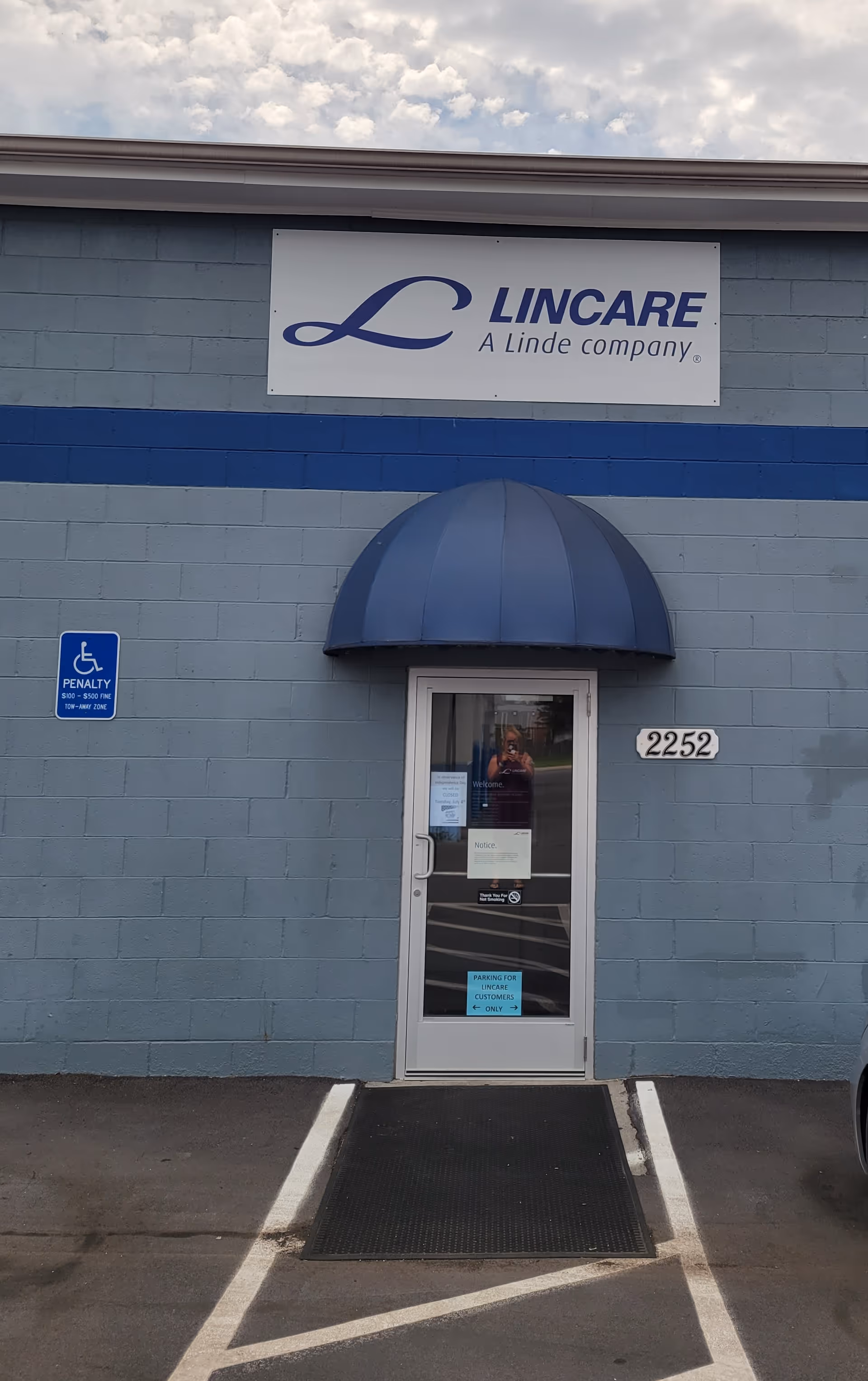 Exterior view of LINCARE building with glass door under blue curved awning and handicap sign.