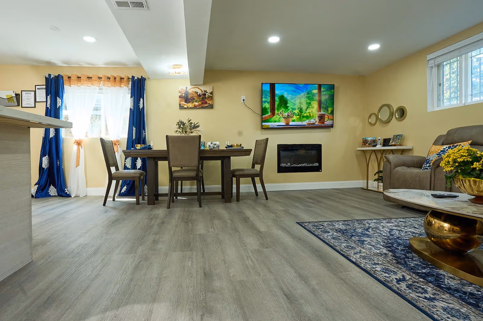 Open living area with dining table, chairs, sofa, fireplace, TV, and bright windows.