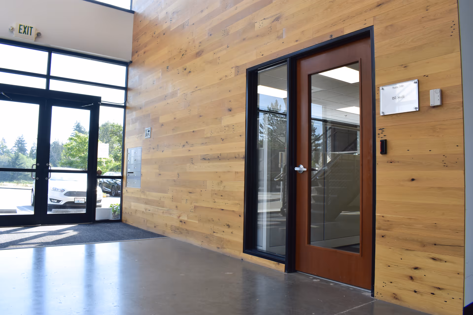 Wood-paneled interior lobby with glass door, exit sign, and view of outside parking.