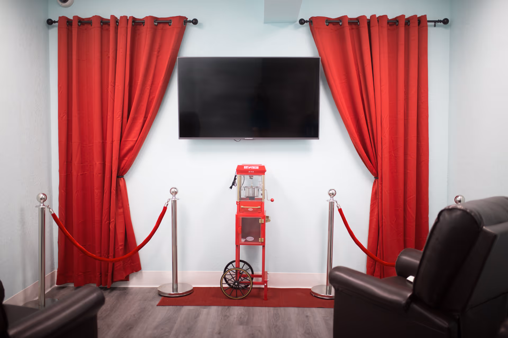 Interior lounge with red curtains, a wall TV, and a red popcorn cart between stanchions.
