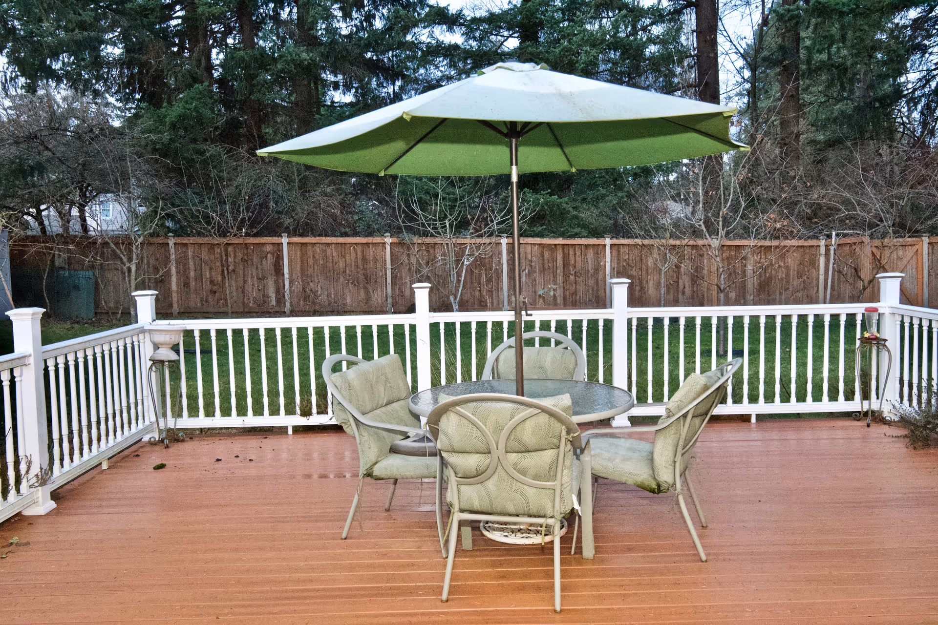 Outdoor deck with a round glass table, surrounding chairs, and a large green umbrella.