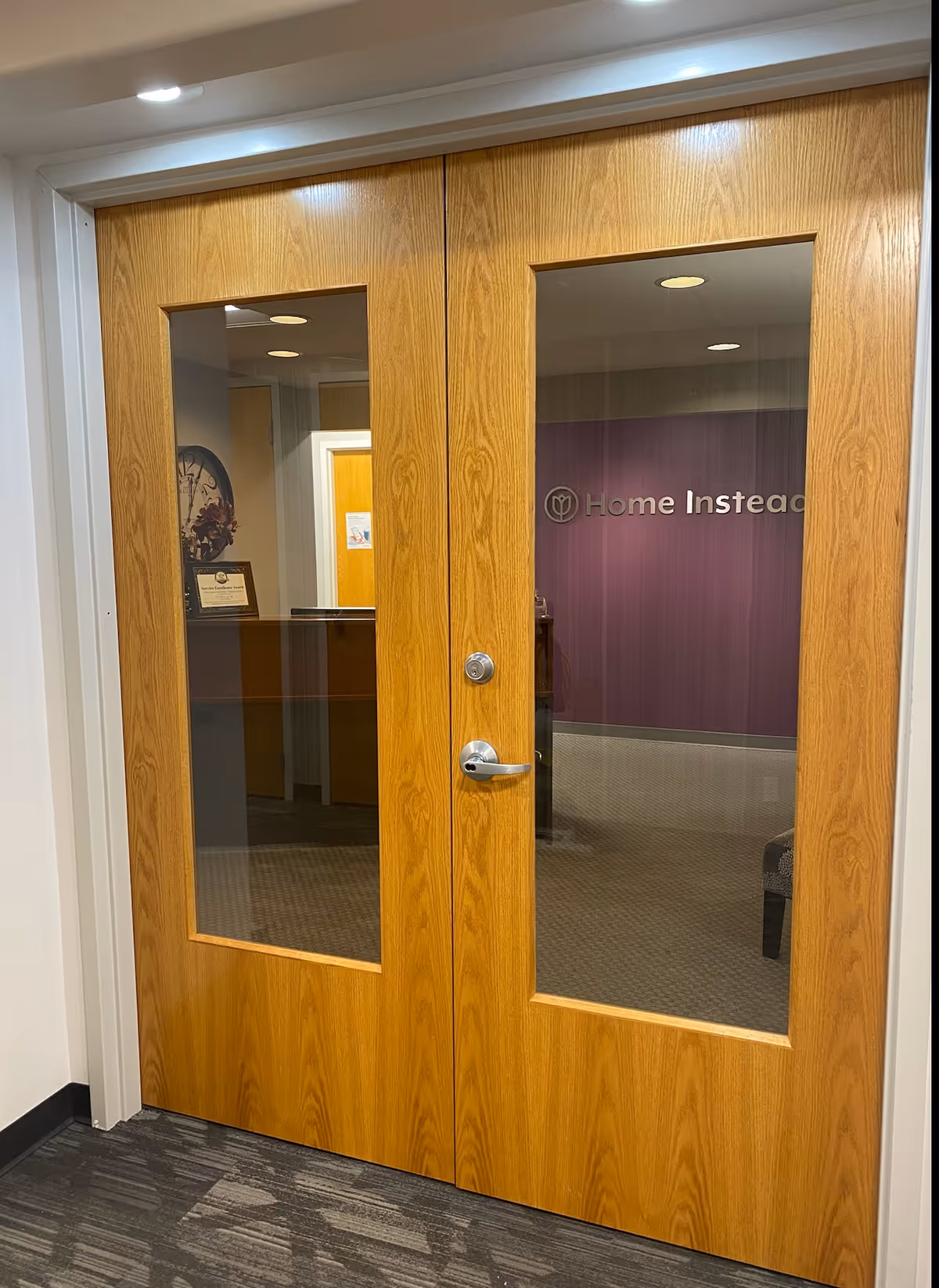 Double wooden doors with glass panels reveal a Home Instead reception lobby.