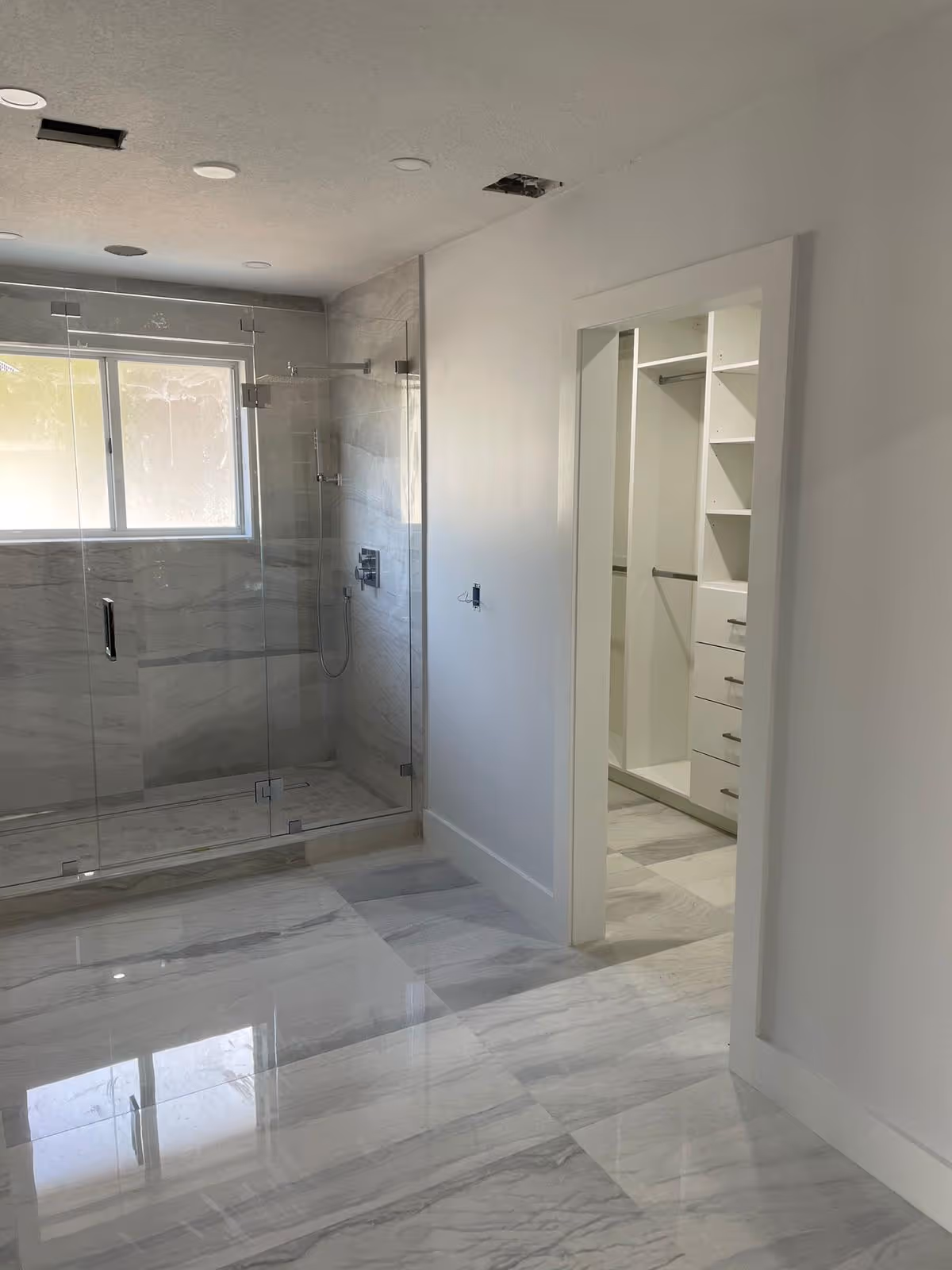 Modern bathroom features a glass-enclosed shower and marble flooring with a walk-in closet nearby.