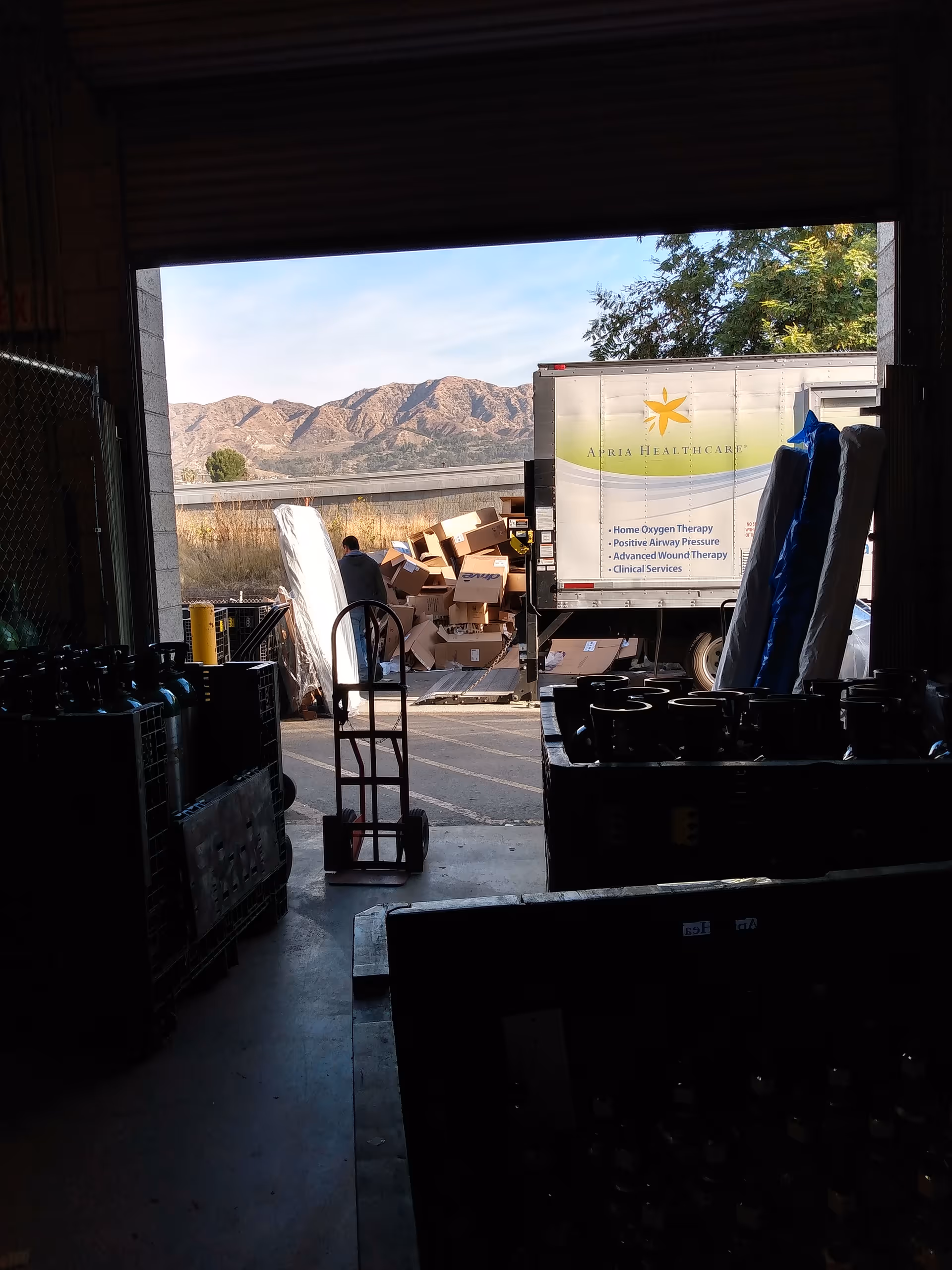 Warehouse loading dock with stacked boxes and an Apria Healthcare truck.