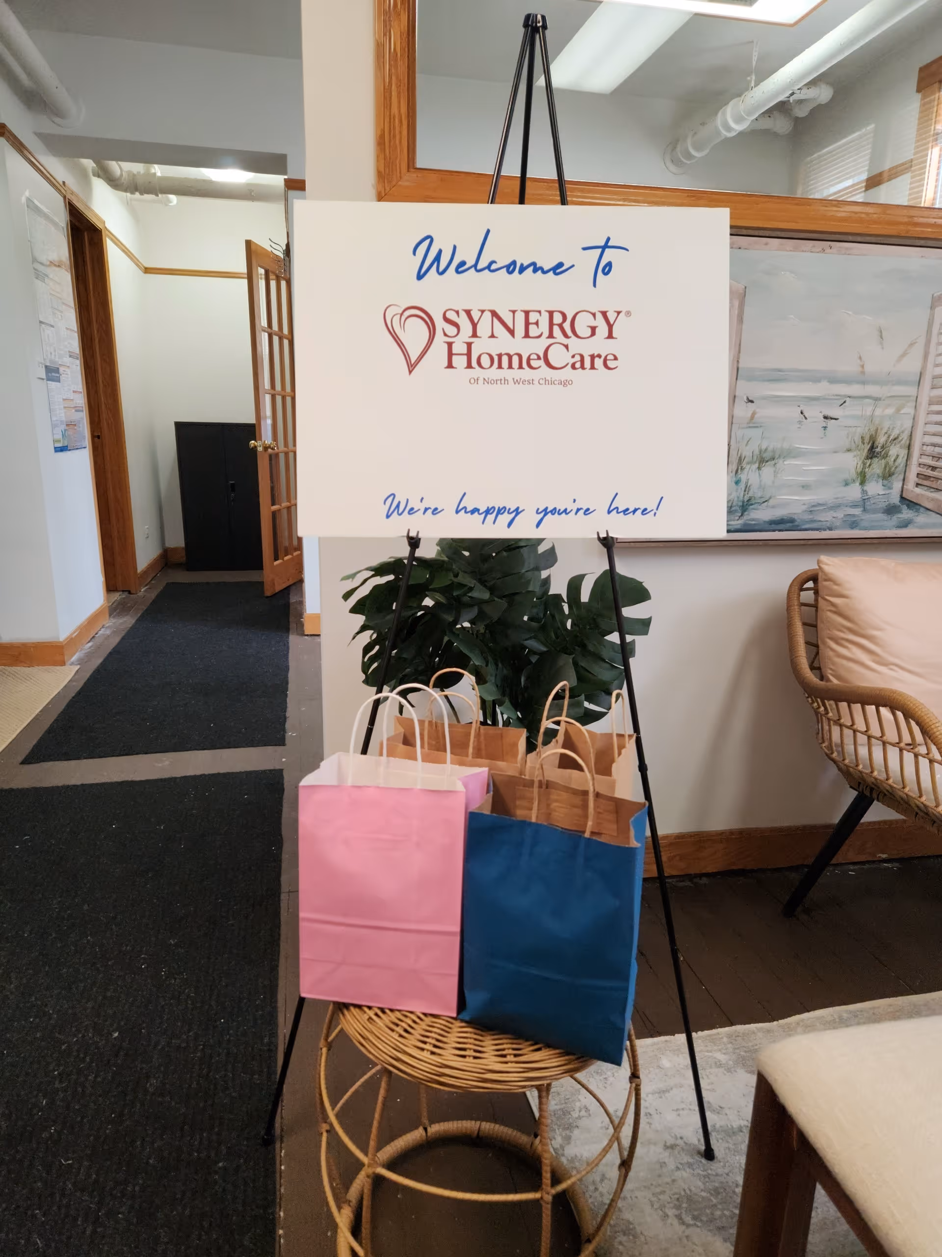 Lobby sign welcomes visitors to Synergy HomeCare with gift bags nearby.
