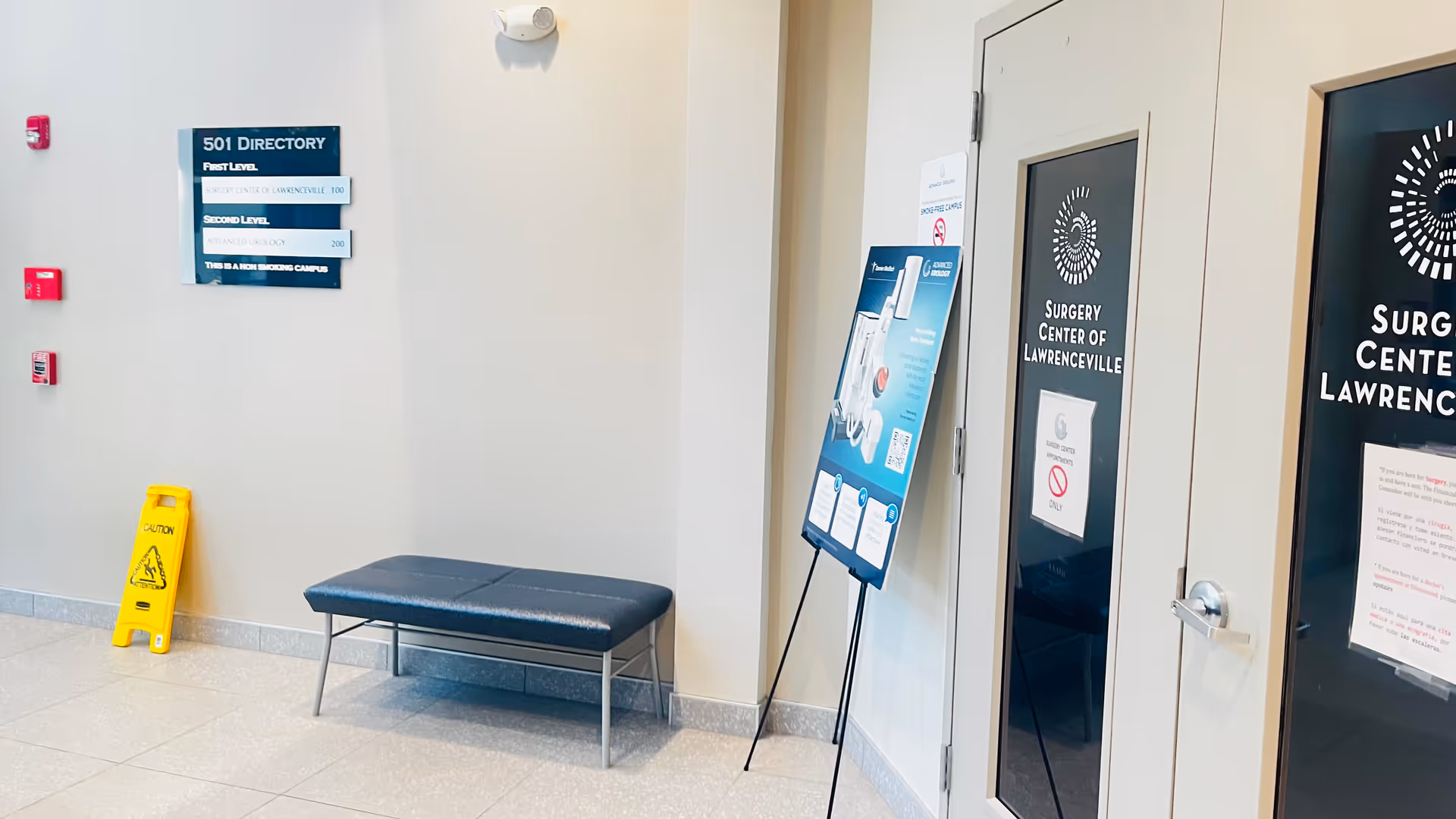Interior hallway with bench, yellow caution sign, and surgery center doors.