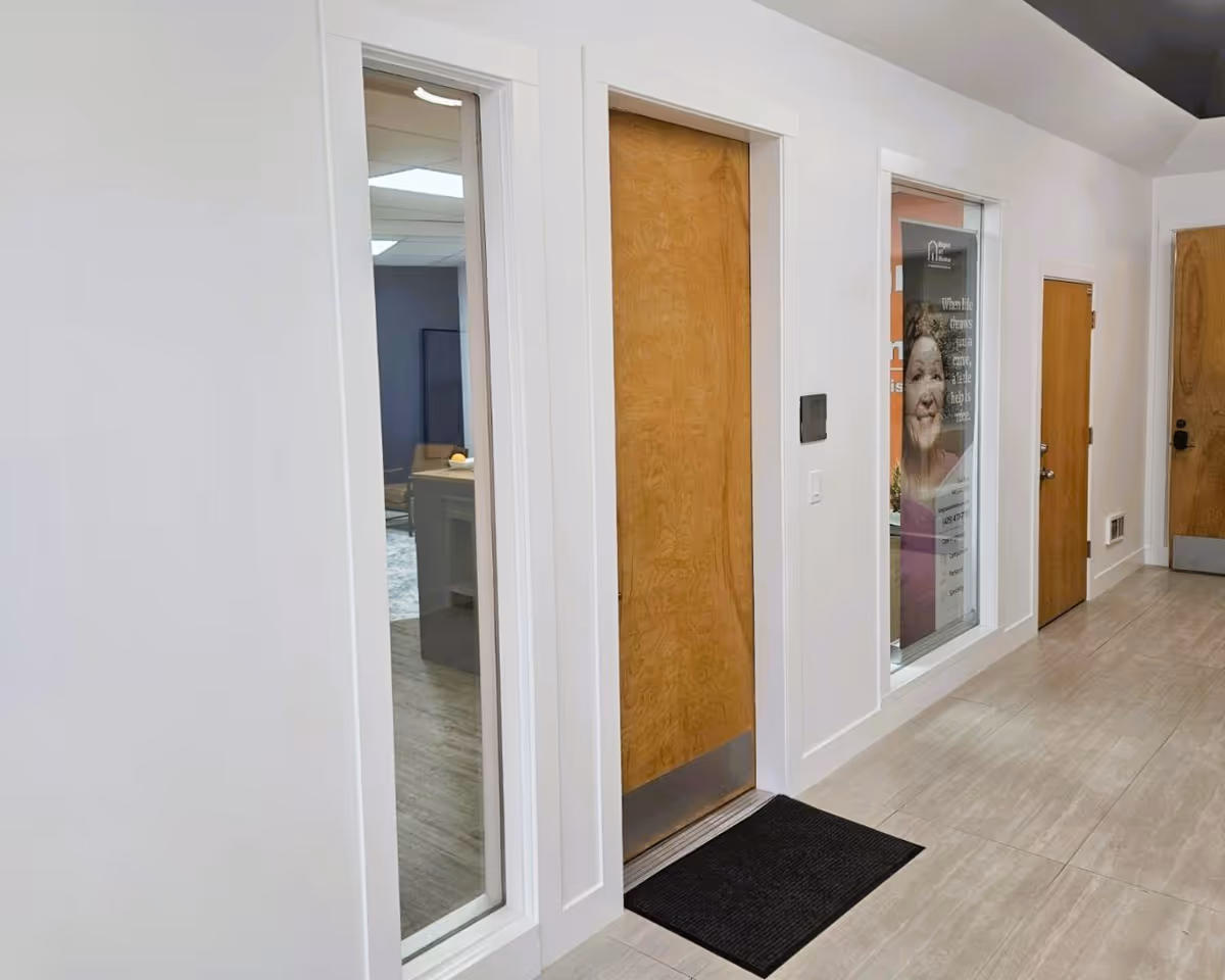 Interior hallway of a senior living facility with wooden doors and a glass display window.