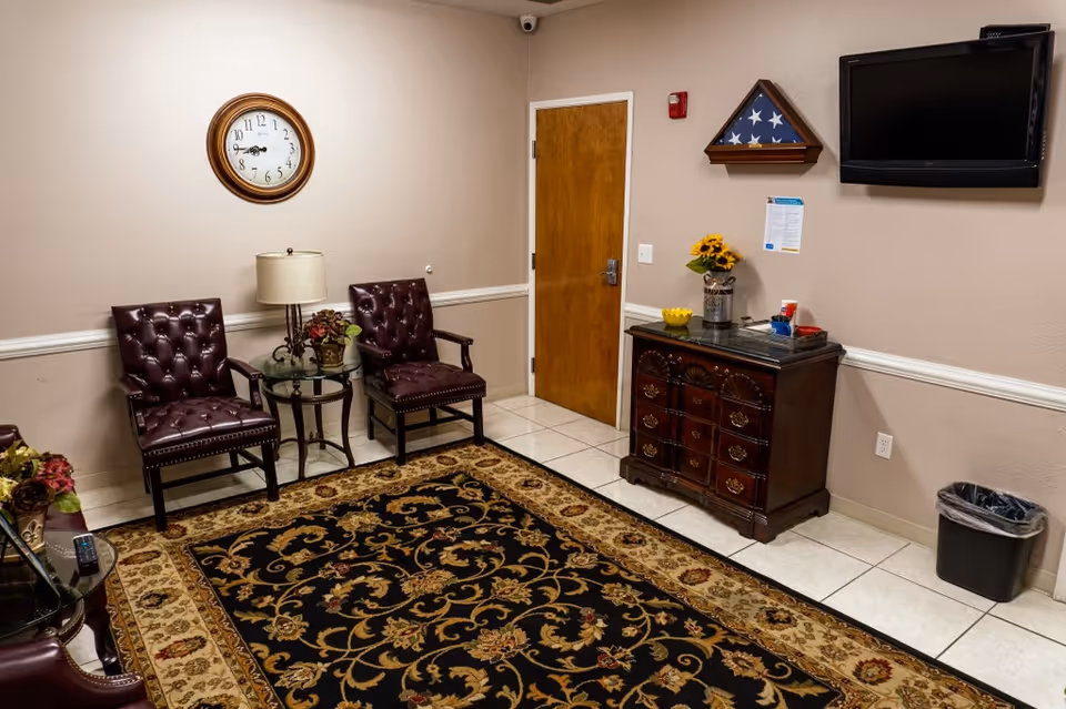 A waiting area with two burgundy chairs, a patterned rug, wall clock, and a wooden cabinet.