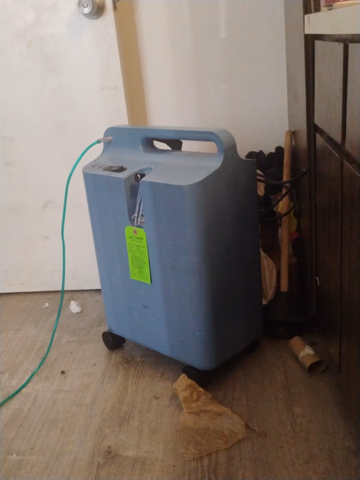 Blue portable oxygen concentrator on wheels in a cluttered interior room.