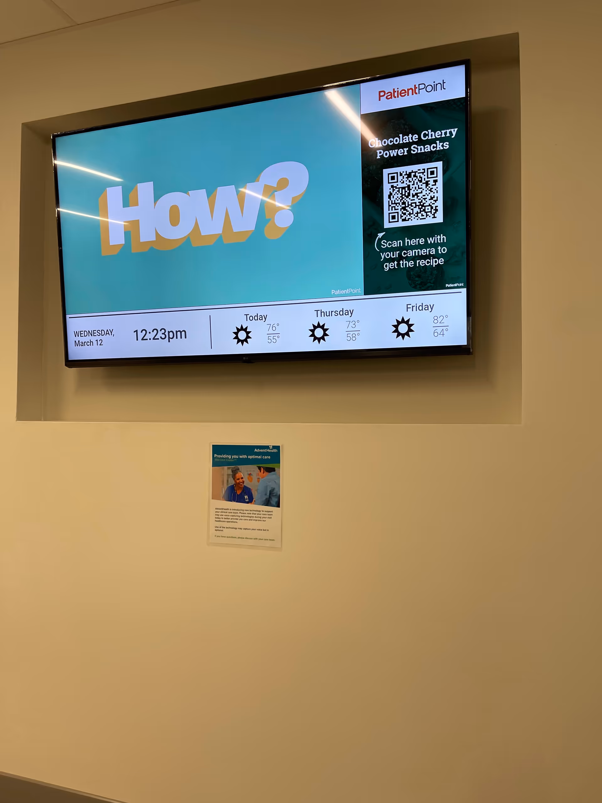 Large wall-mounted monitor displays 'How?' graphic and weather info in a hallway.