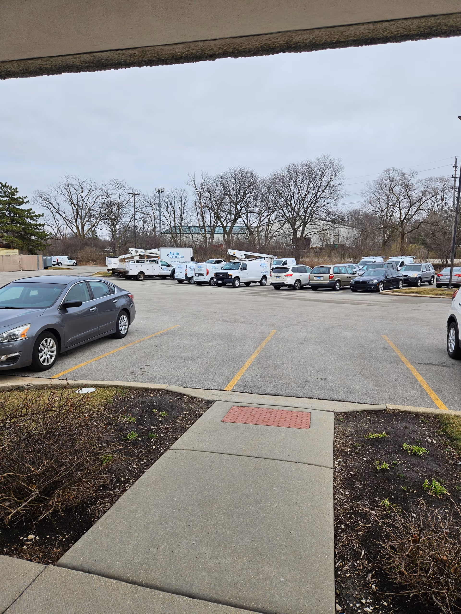 Parking lot outside a facility with vans, cars, and leafless trees.