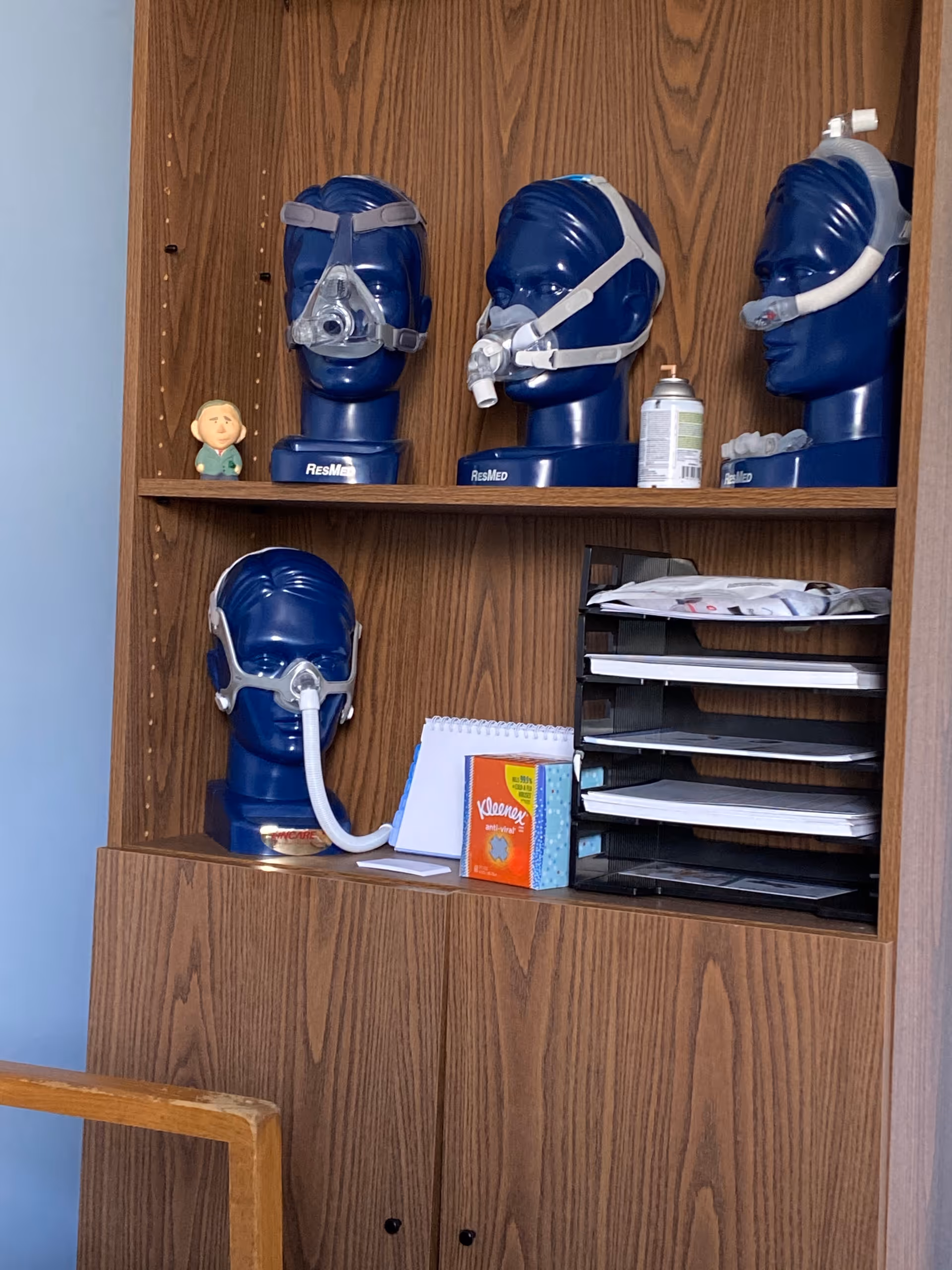 Wooden cabinet filled with blue CPAP masks and office supplies.